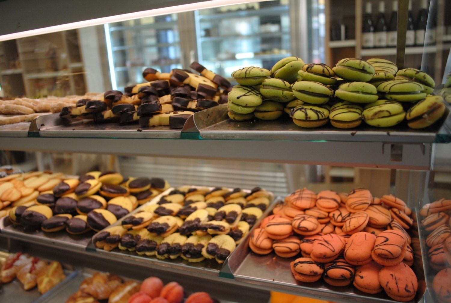 Macarons colorati assortiti disposti su scaffali espositivi in una vetrina da pasticceria.