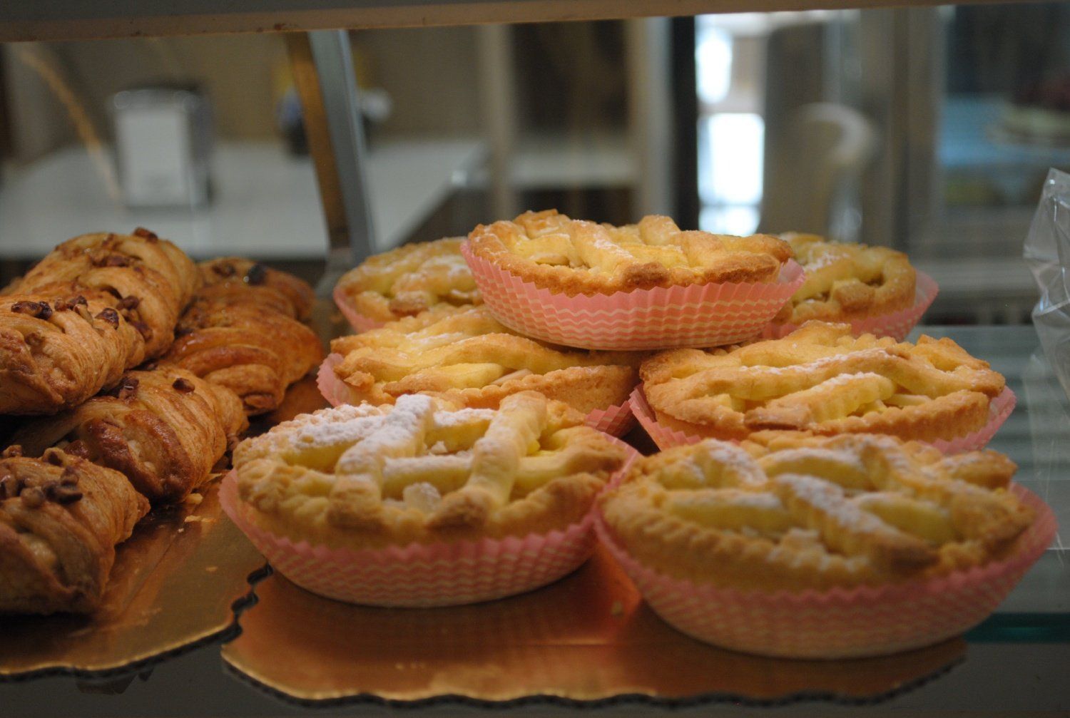 Vassoio di crostatine di frutta rosa pastello accanto a croissant in una vetrina di pasticceria.
