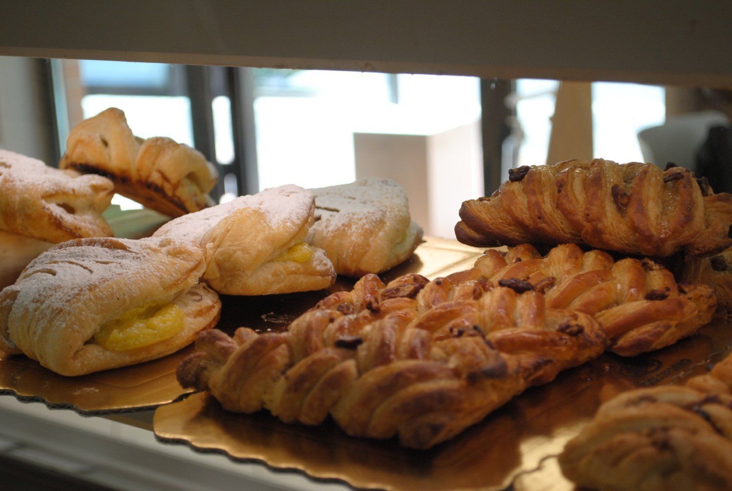 Assortimento di pasticcini e croissant esposti su vassoi al bancone di una pasticceria.