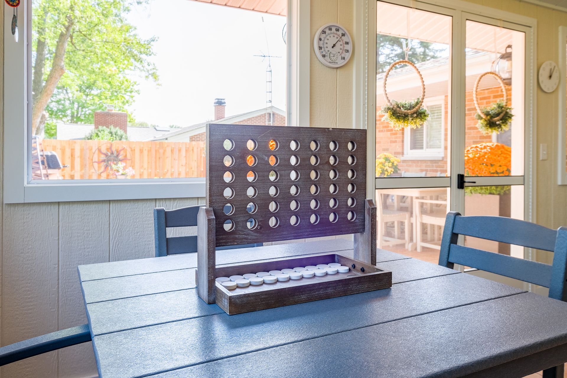 Connect Four game on a gray table in a sunroom with a view of a backyard.