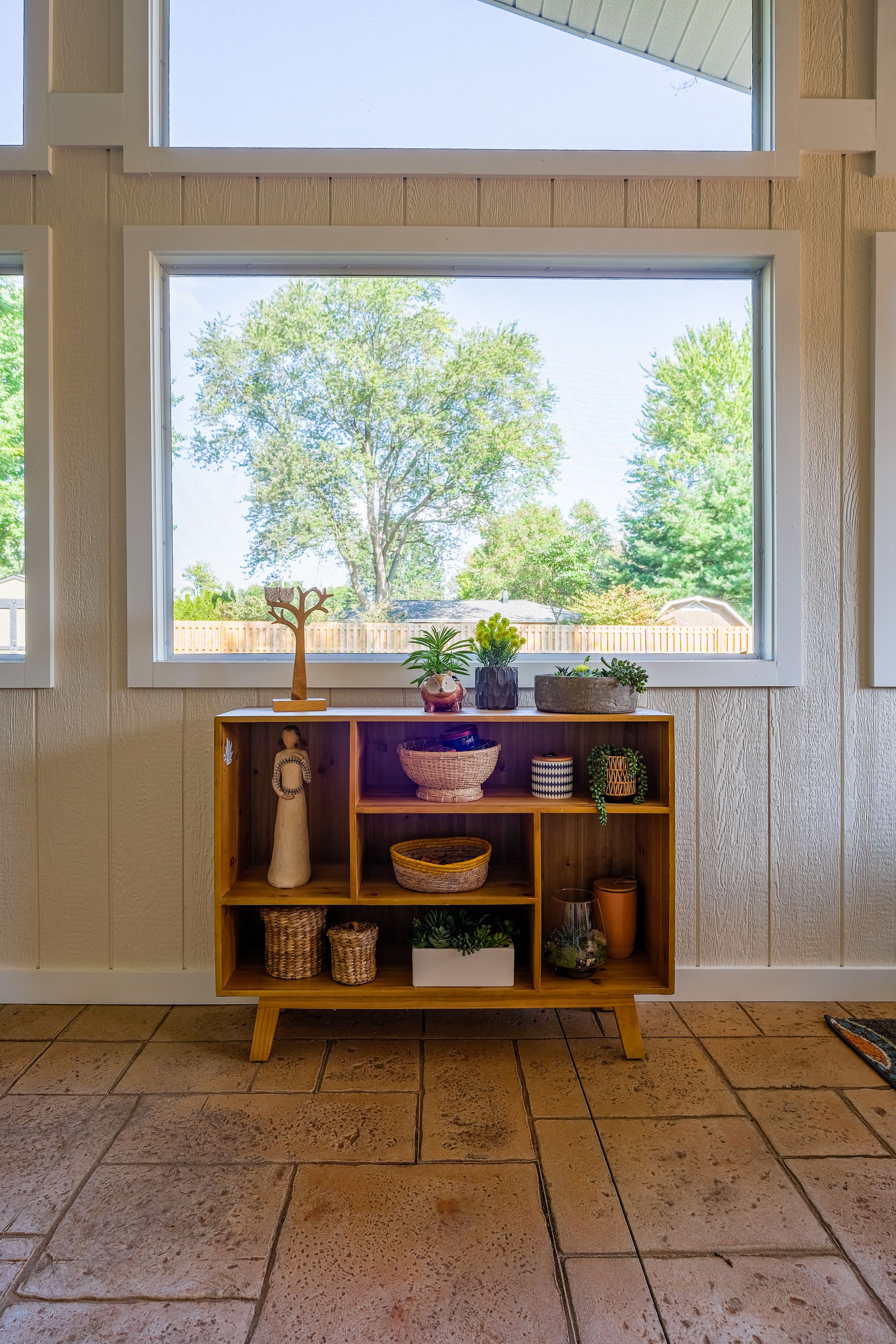 Wooden bookshelf with decor in front of a window overlooking greenery.