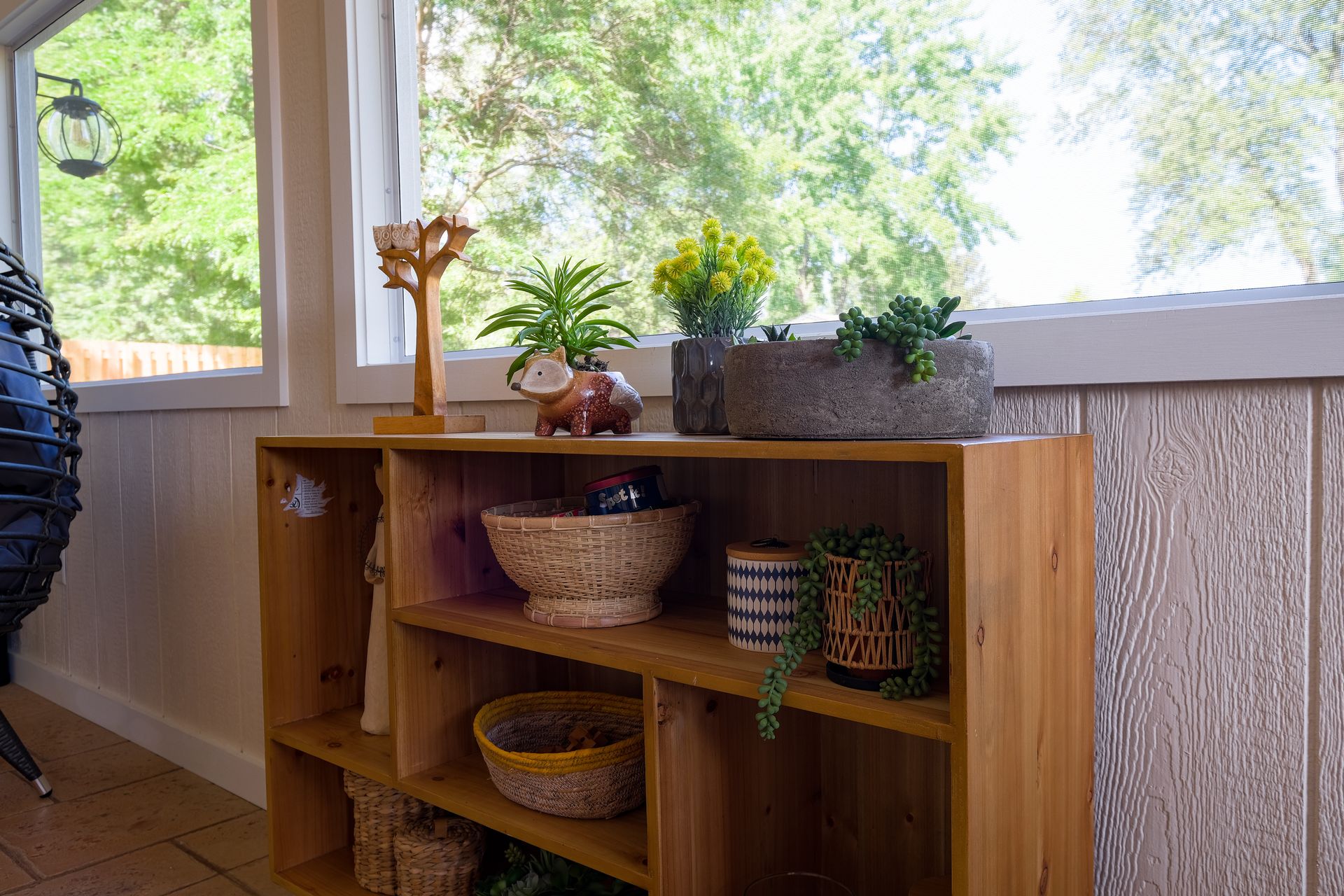 Wooden shelf with plants and decorative items in front of a window.
