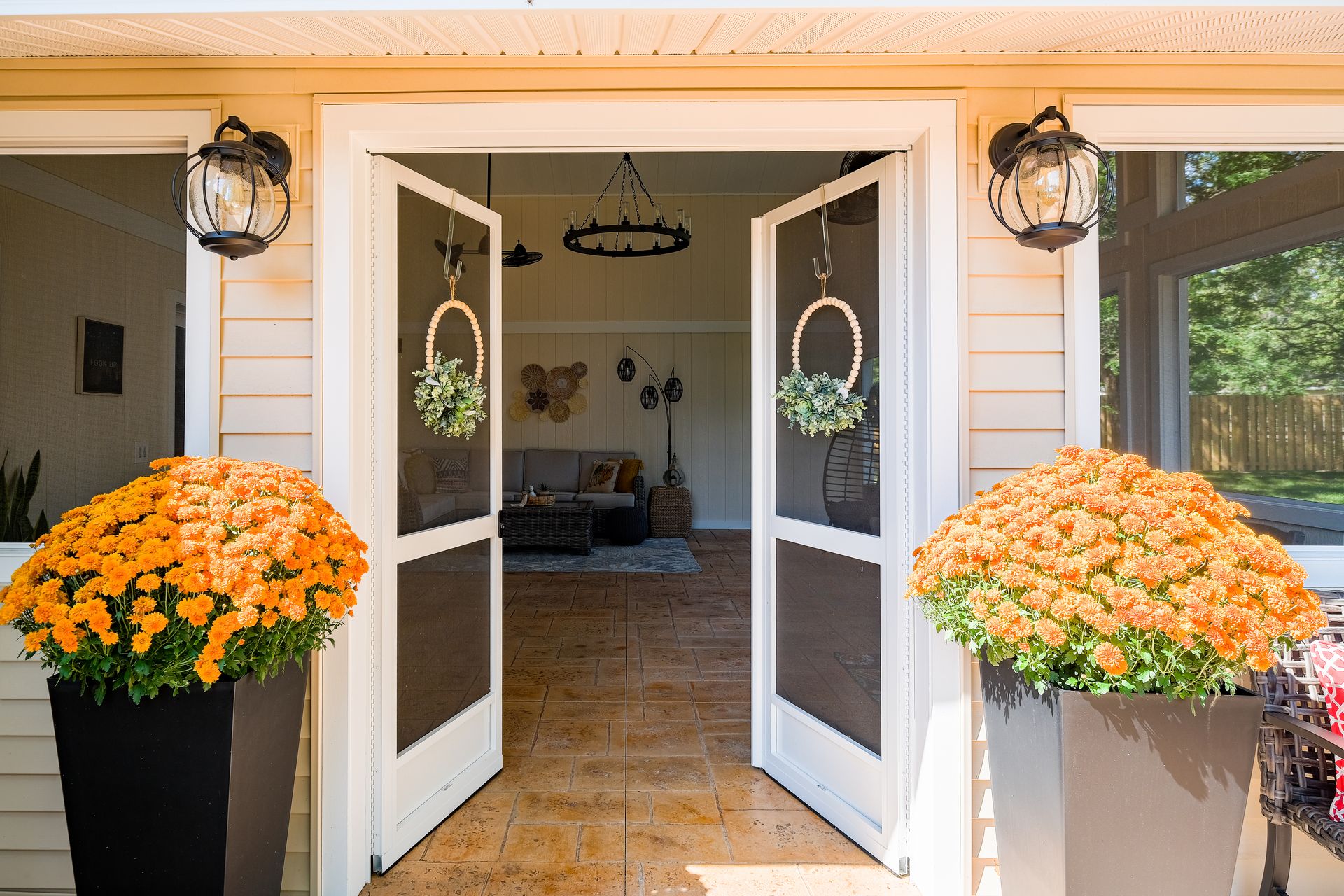 Open front doors with orange mums in large planters. Two wreaths hang from the doors.