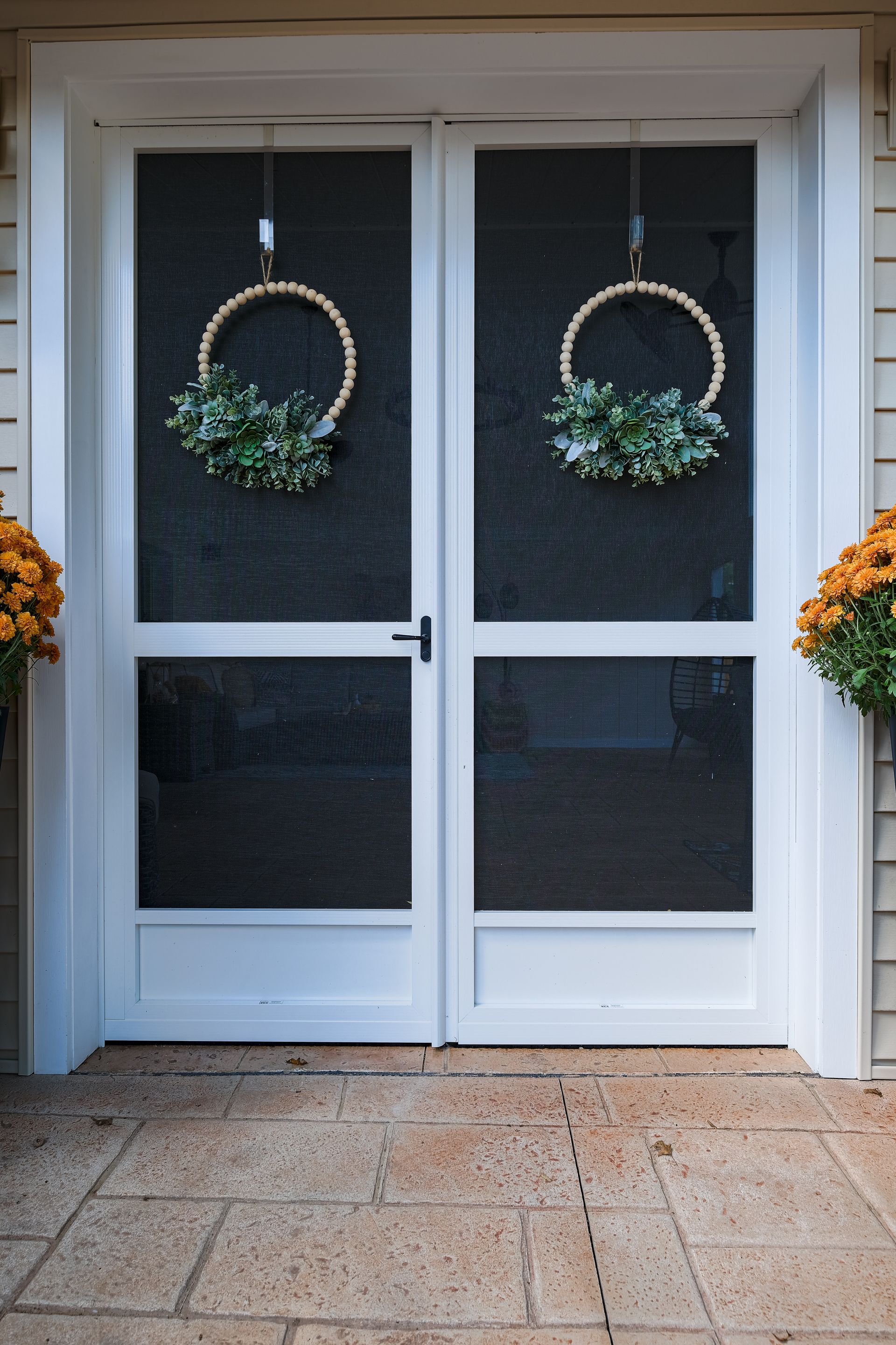 White screen doors decorated with wreaths and flanked by orange flowers.