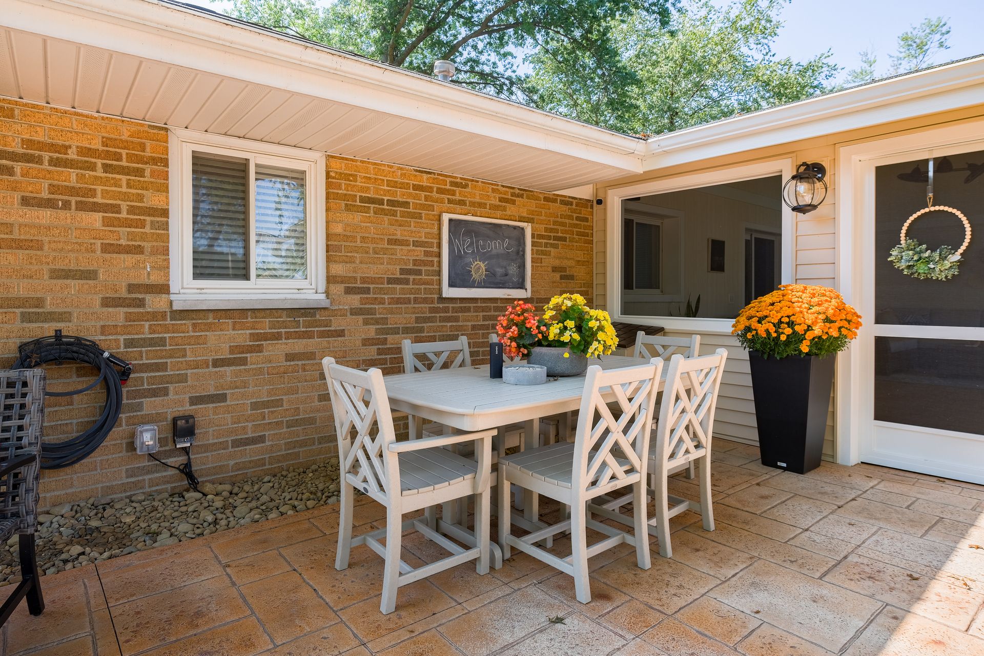 Patio with table and chairs, brick wall, potted flowers, and screened door.