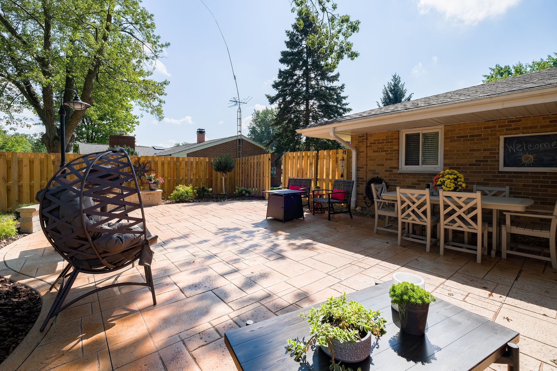 Spacious backyard patio with seating areas, brick house, and trees under a sunny sky.