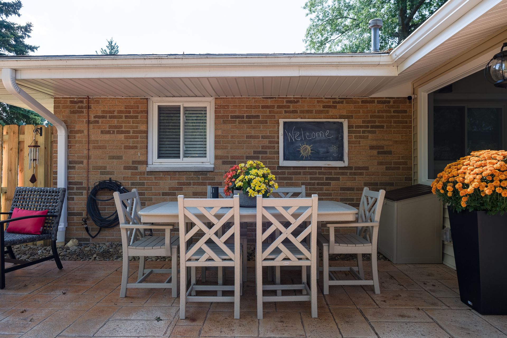Outdoor patio with a table and chairs under a brick wall, decorated with flowers.