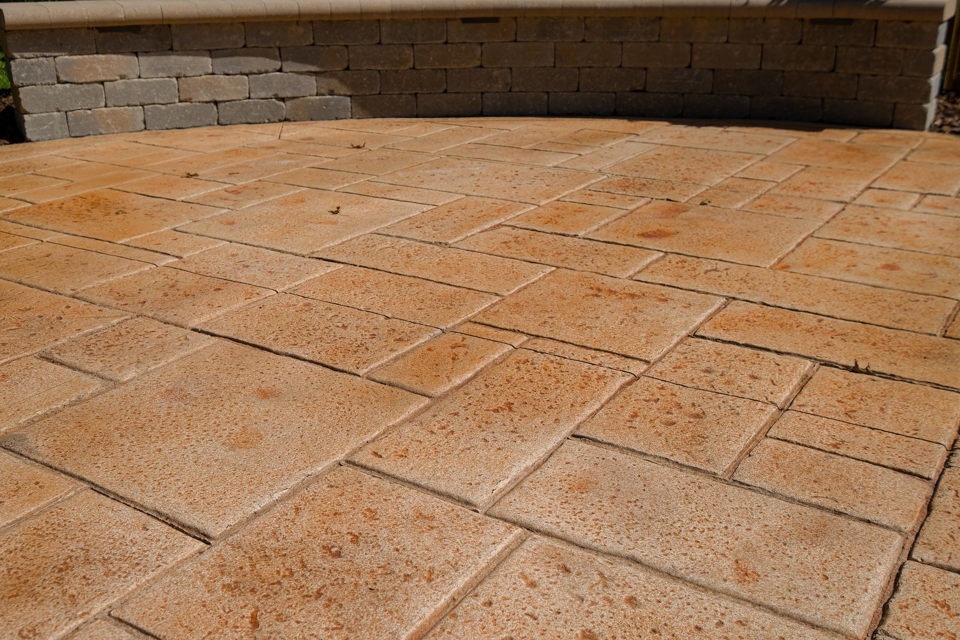 Brick patio with tan/brown stamped concrete, with matching retaining wall.