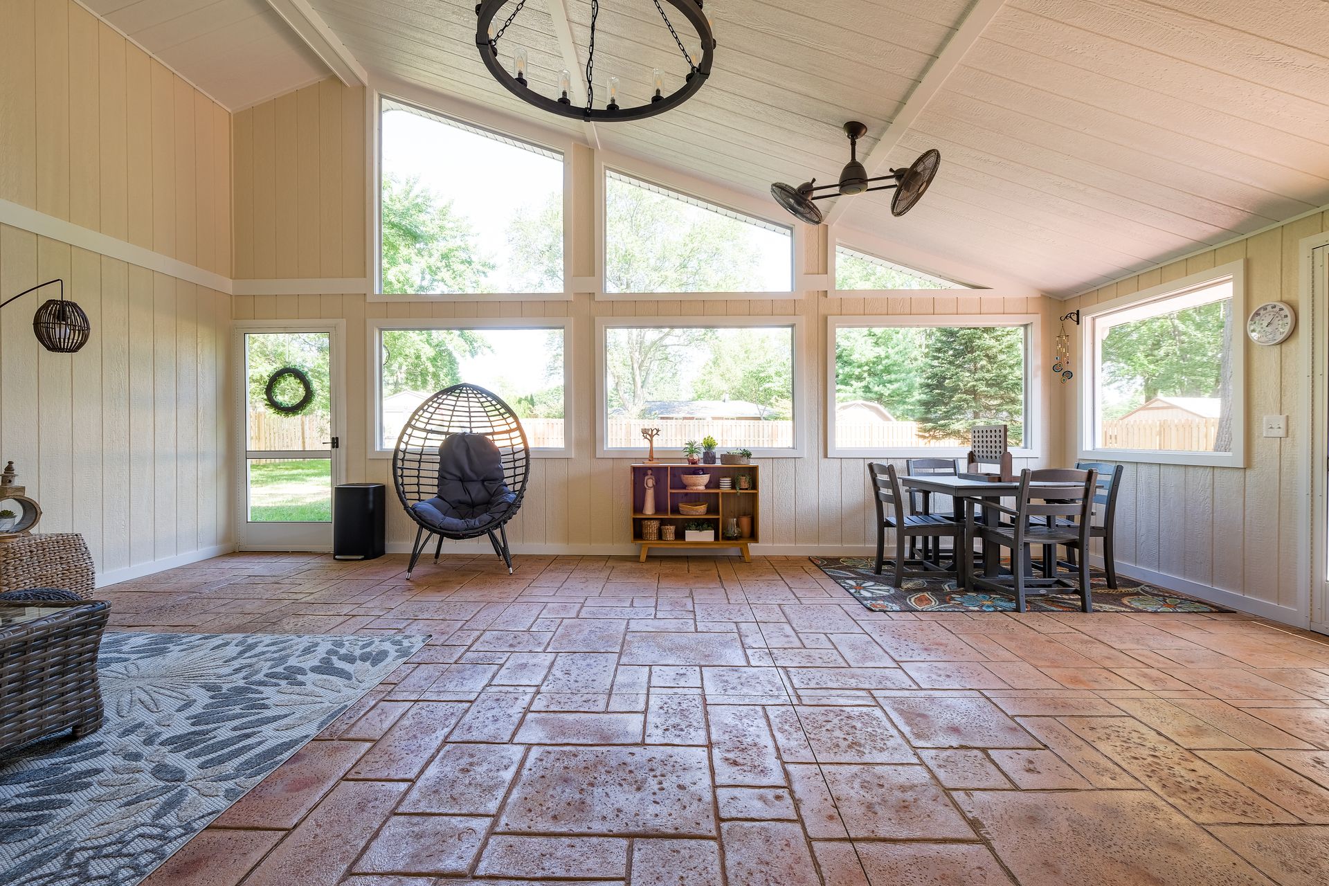 Sunroom with large windows, an egg chair, dining table, and stone-like flooring.