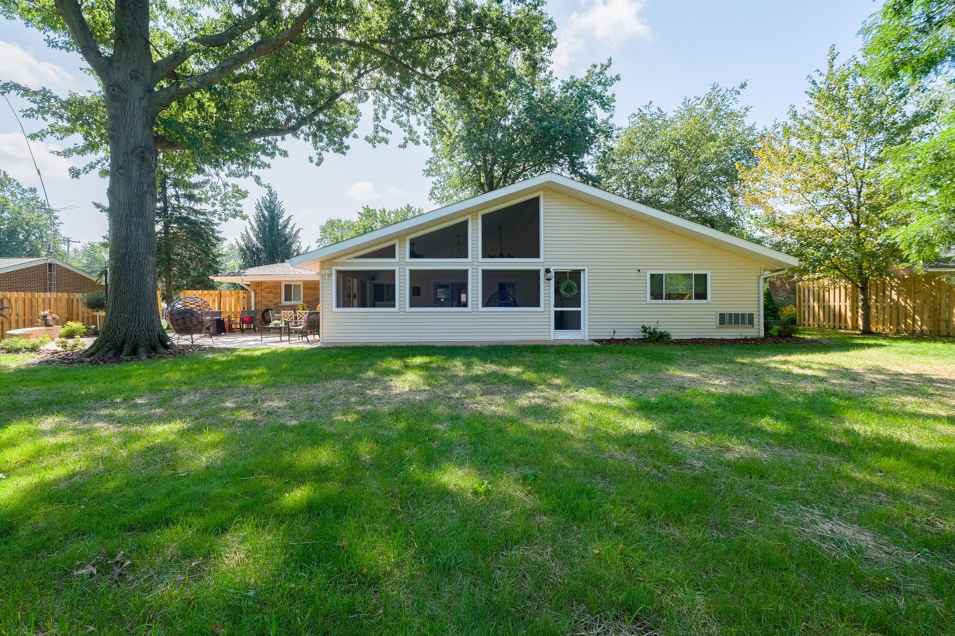Backyard view of a one-story house with a large screened-in porch, surrounded by trees and a green lawn.
