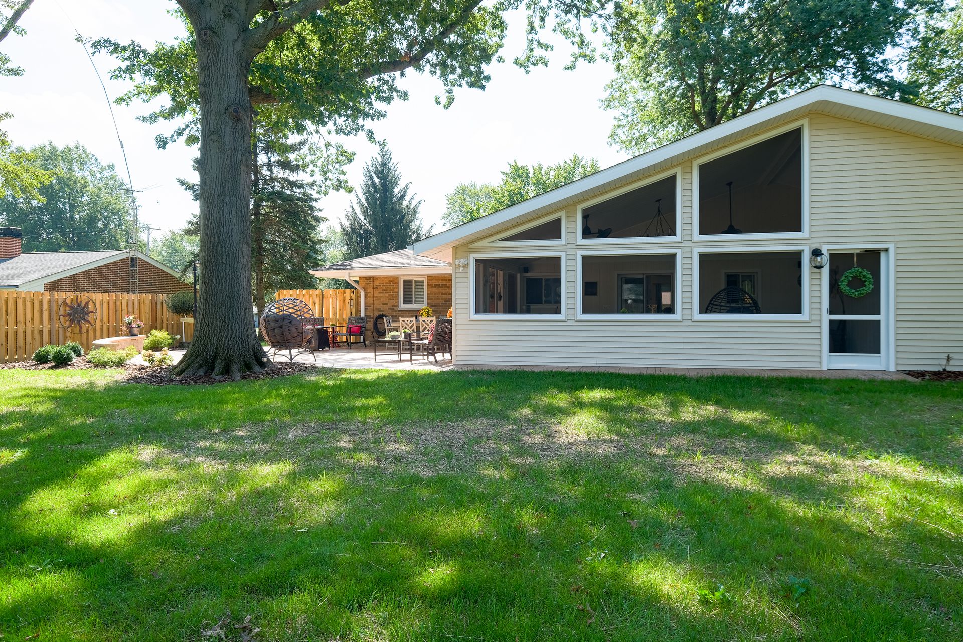 Backyard with house, large windows, patio, and green lawn on a sunny day.