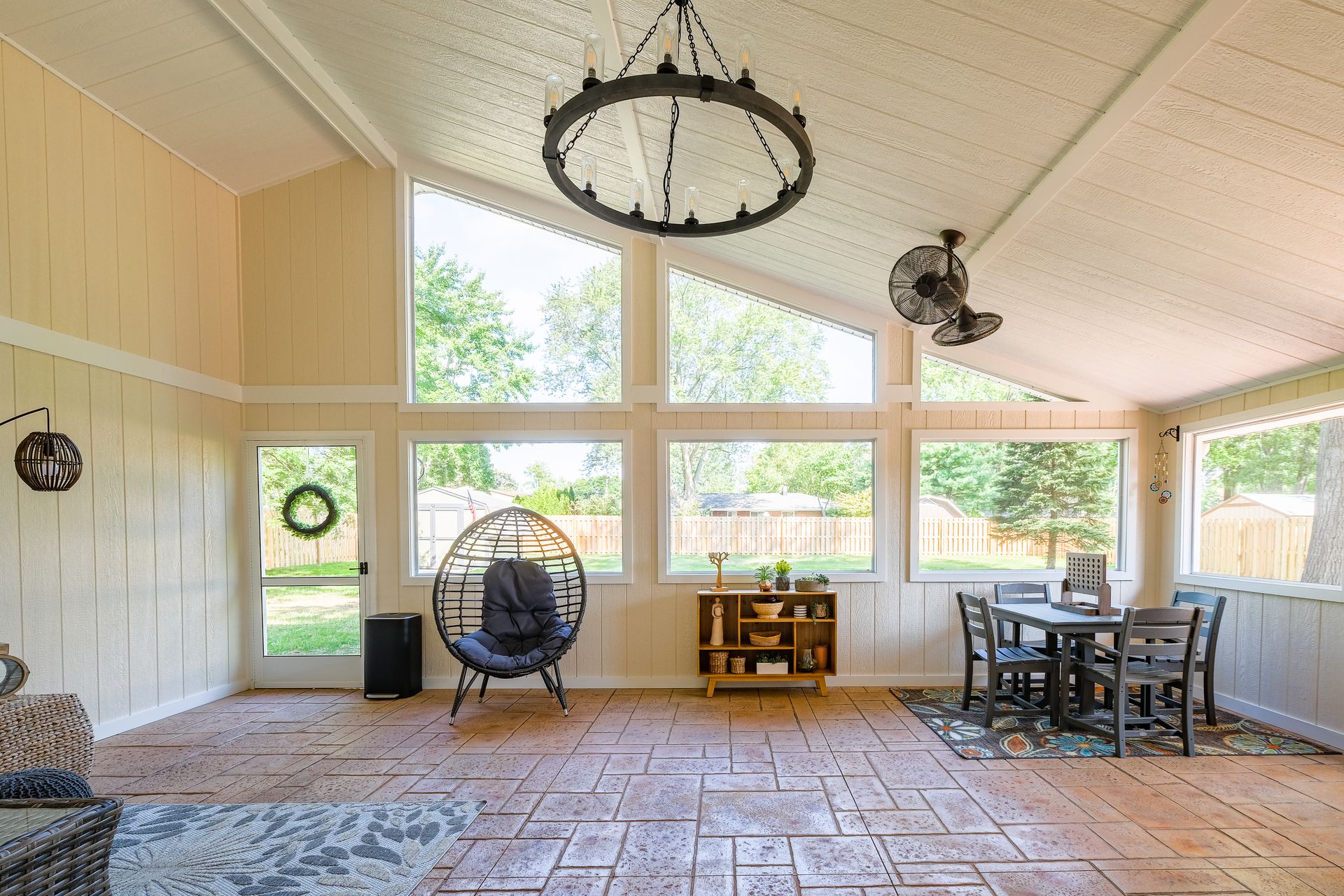 Sunroom with large windows, an egg chair, dining table, and decorative chandelier.