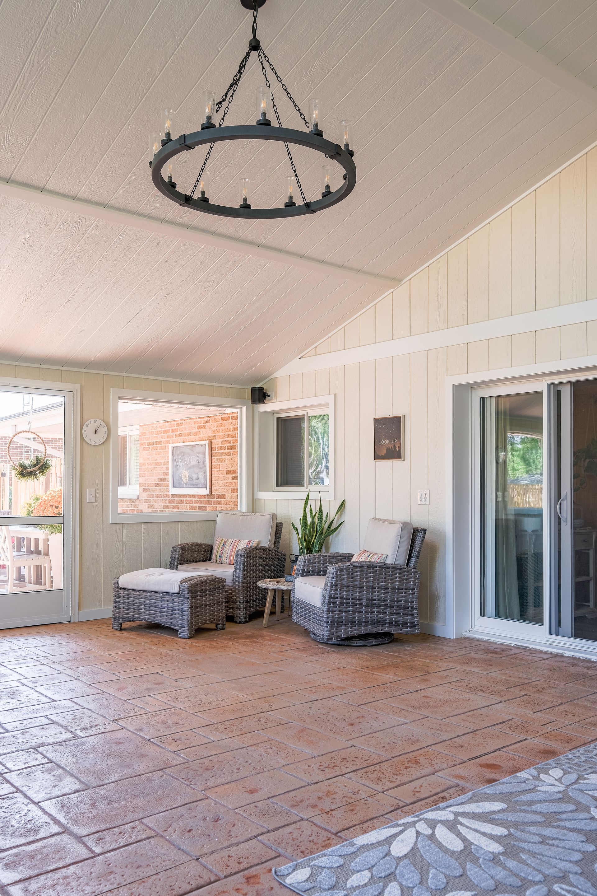 Sunroom with brick floor, wicker furniture, and a large chandelier.