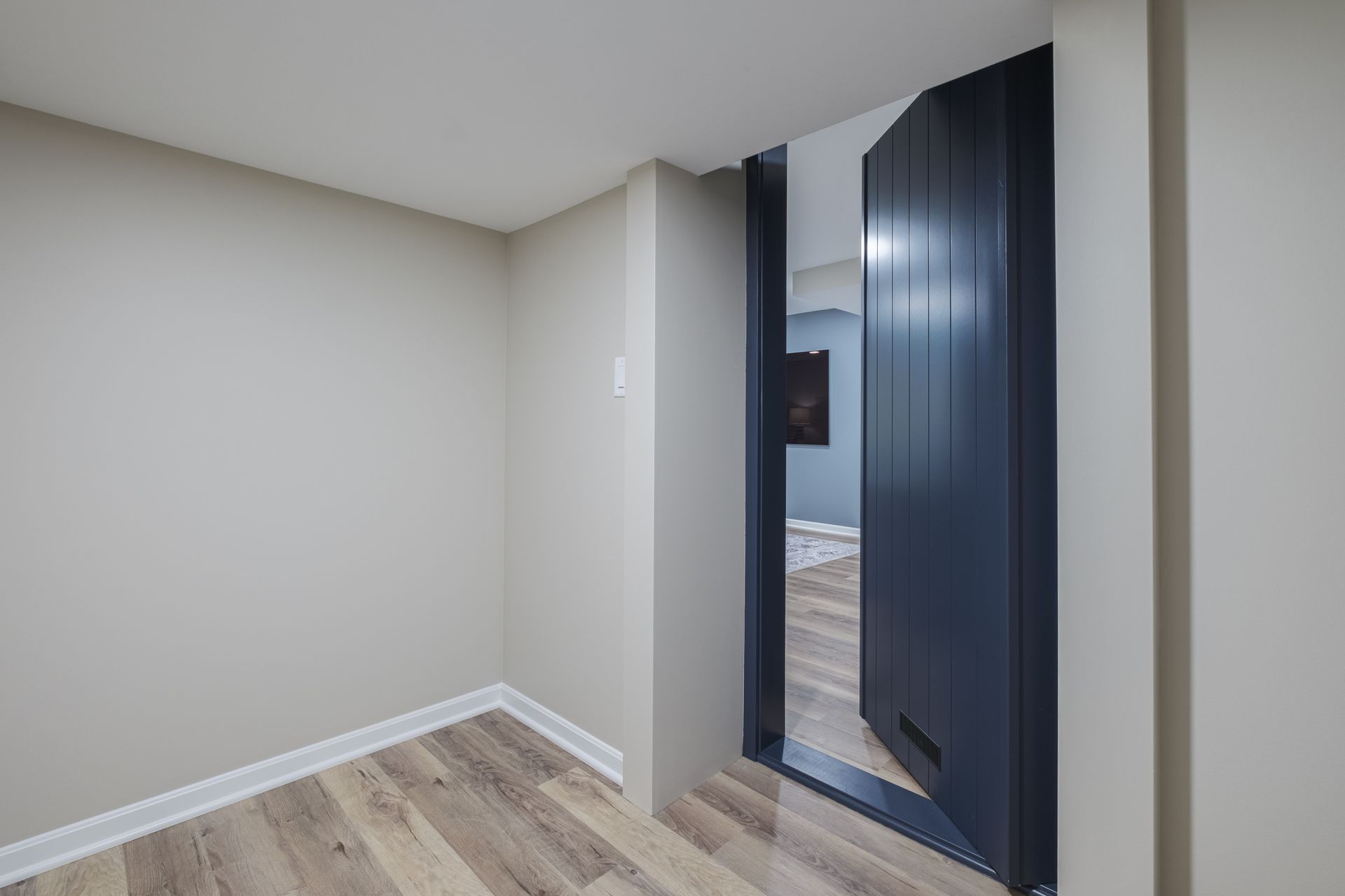 An empty room with hardwood floors and a blue door leading to a living room.