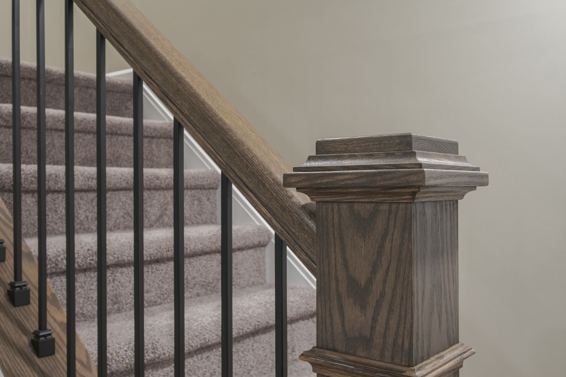 A close up of a wooden railing on a staircase with carpeted steps.