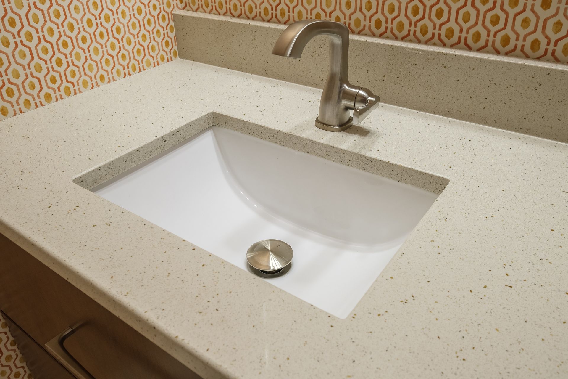Bathroom sink with light speckled countertop, faucet, and patterned yellow and orange wall.