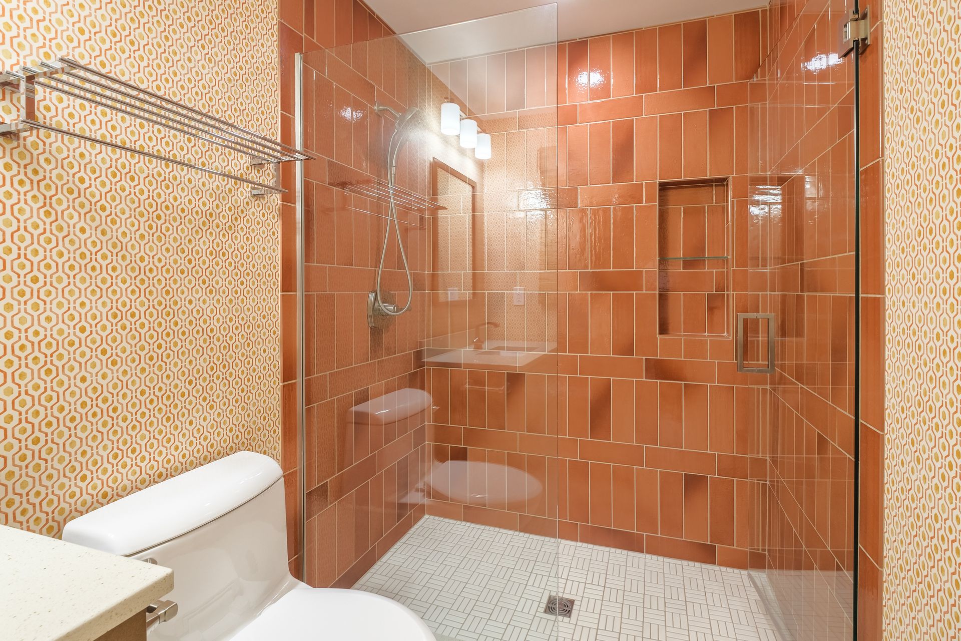 Bathroom with orange tile walls, glass shower door, and white toilet.