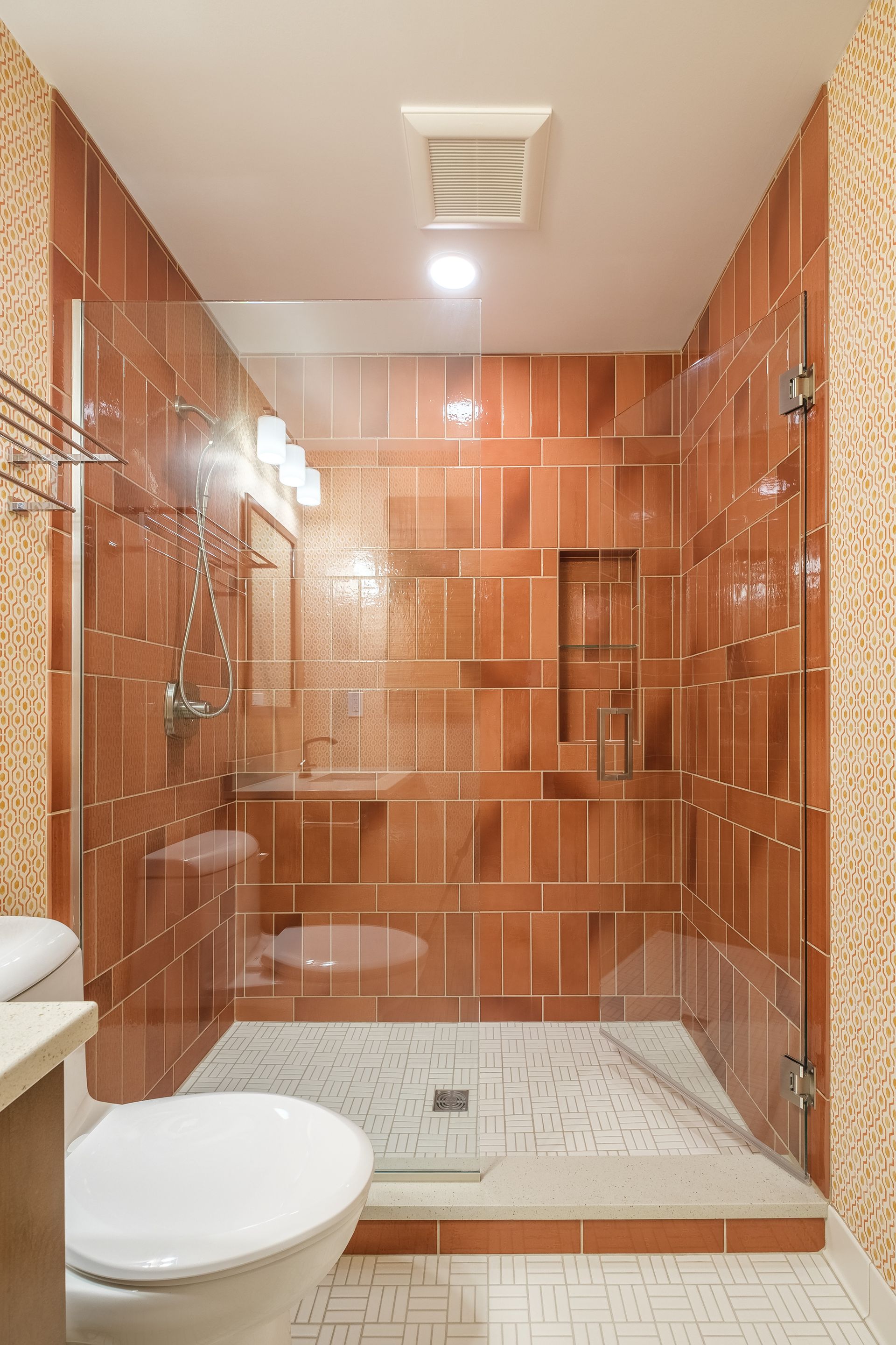 Bathroom with brown tiled shower and white toilet. Clear glass shower door. White and brown tile floors.