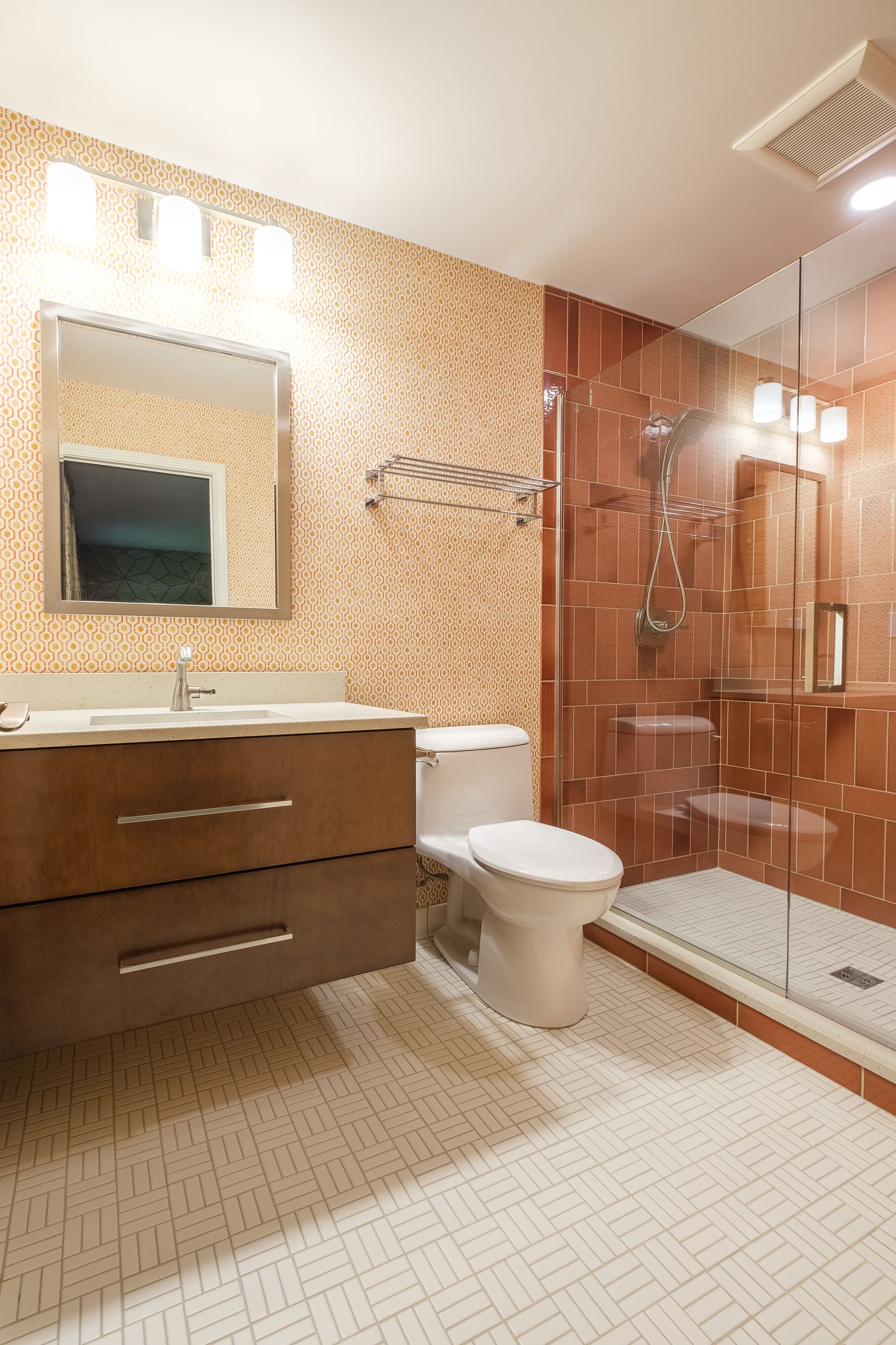 Bathroom with brown tiled walls, white floor, vanity, toilet, and glass shower.