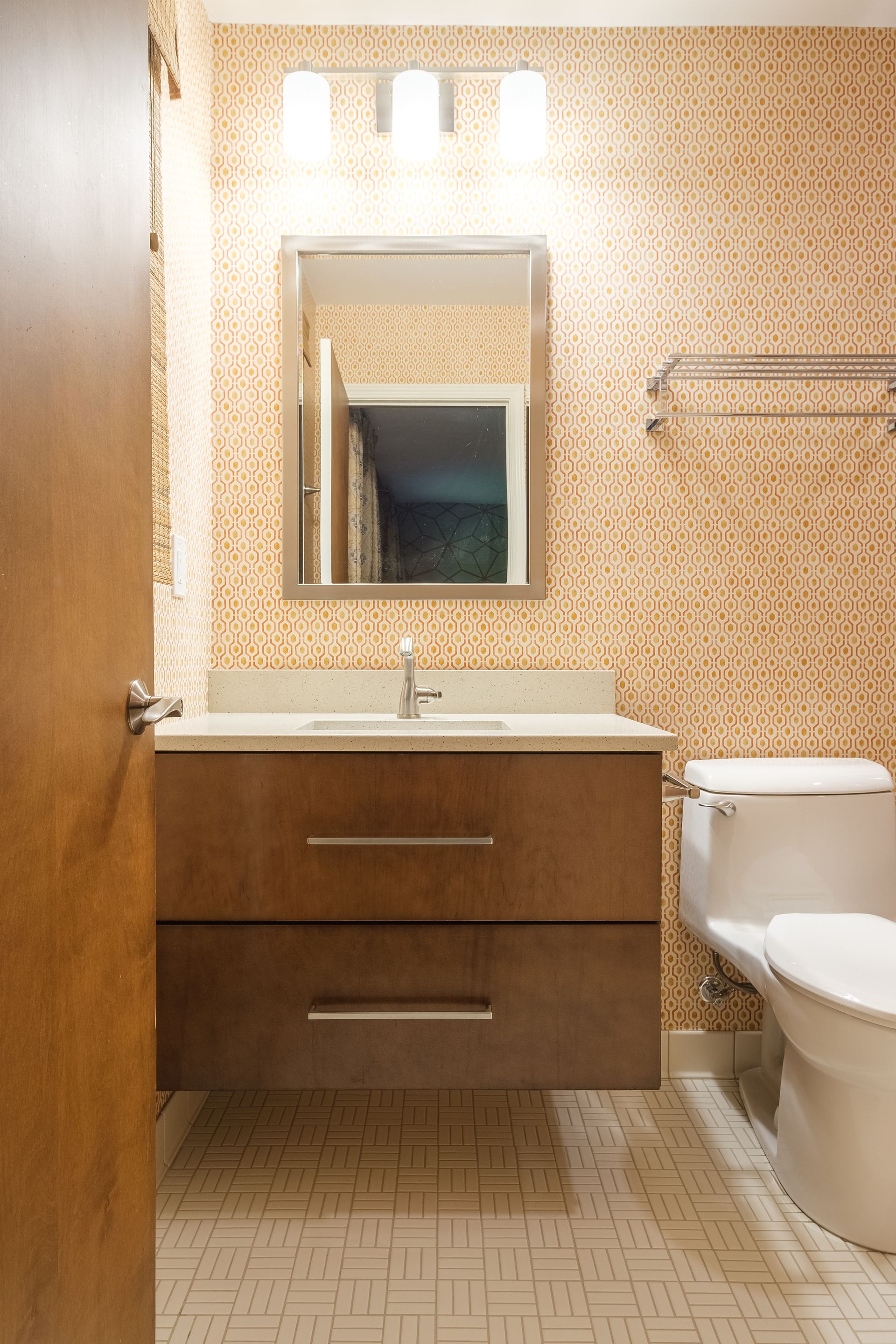 Bathroom with a wooden vanity, a white toilet, patterned wallpaper, and a mirror.