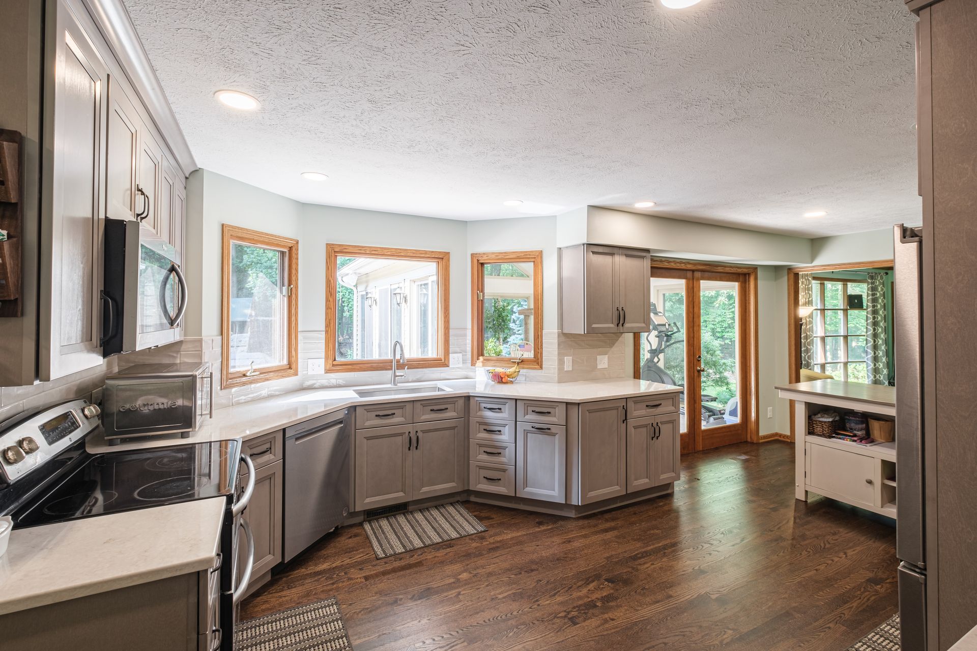 A kitchen with gray cabinets , white counter tops , stainless steel appliances and hardwood floors.
