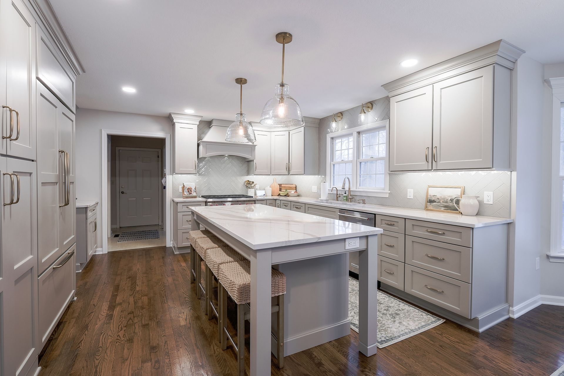 Modern gray kitchen with island, marble counters, wood floors, and pendant lights.