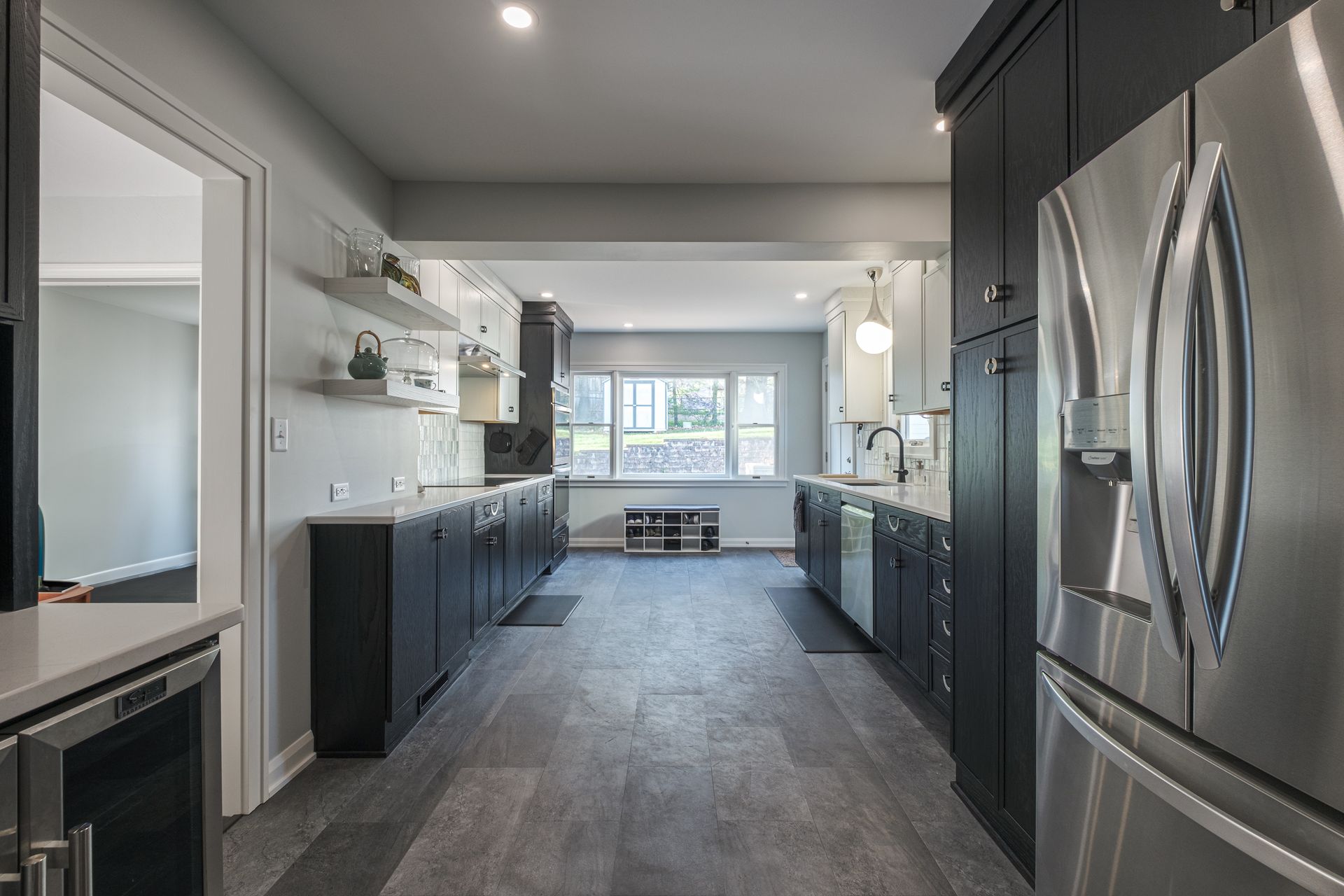Long kitchen with gray floor, black and white cabinets, stainless steel appliances, and a view into the next room.