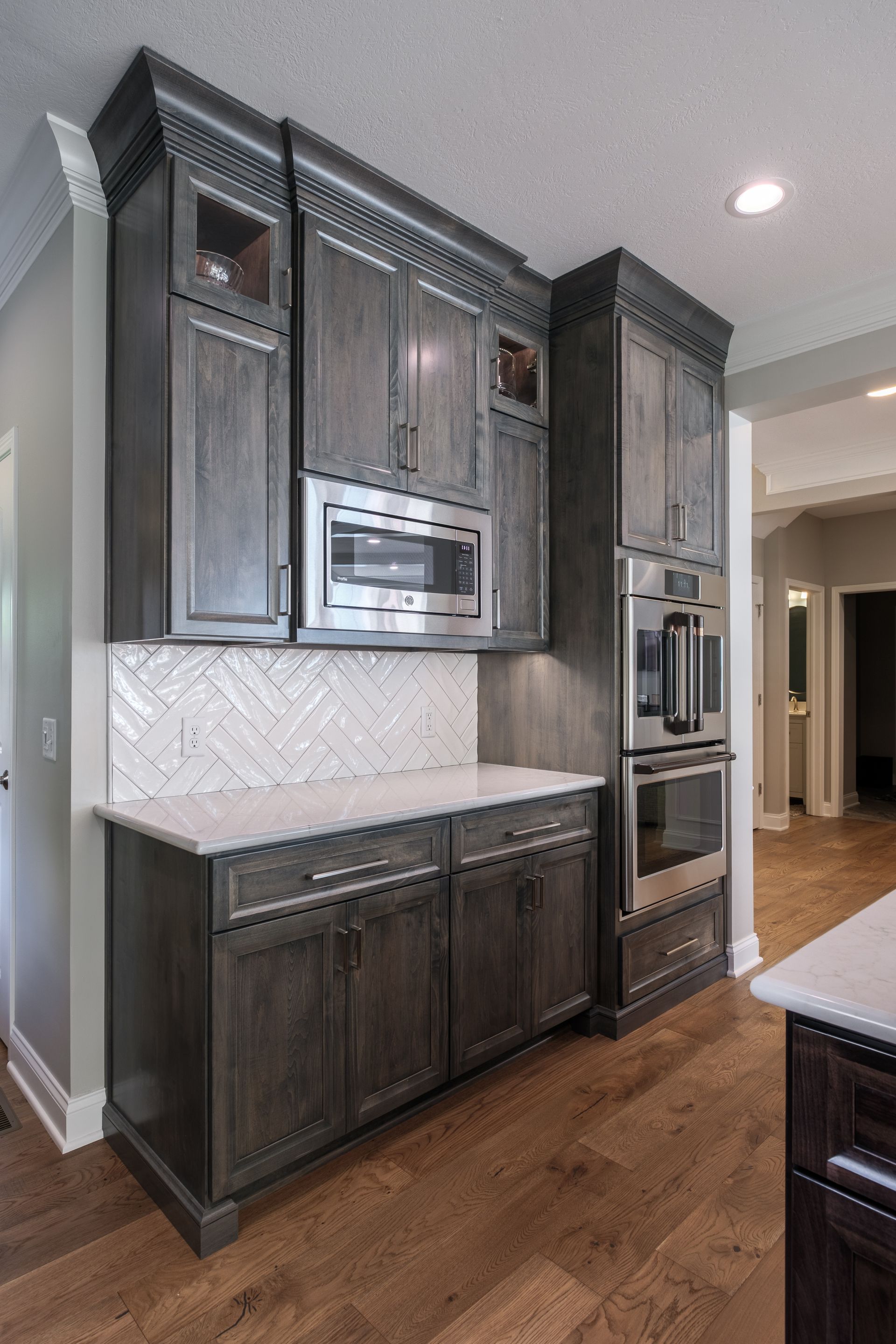 Dark gray kitchen cabinets with a white countertop and herringbone backsplash; built-in appliances.