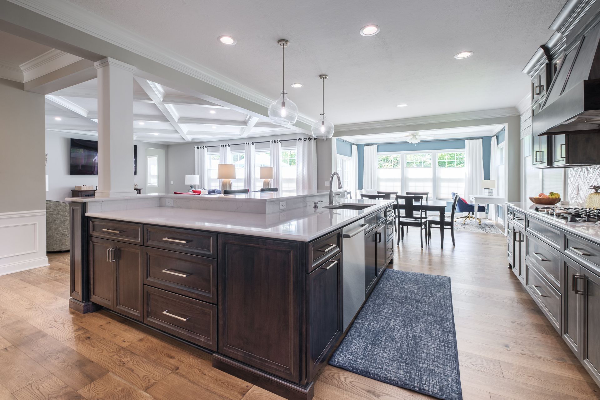 Modern kitchen with dark cabinetry, light countertops, and wood floors. Dining area visible.