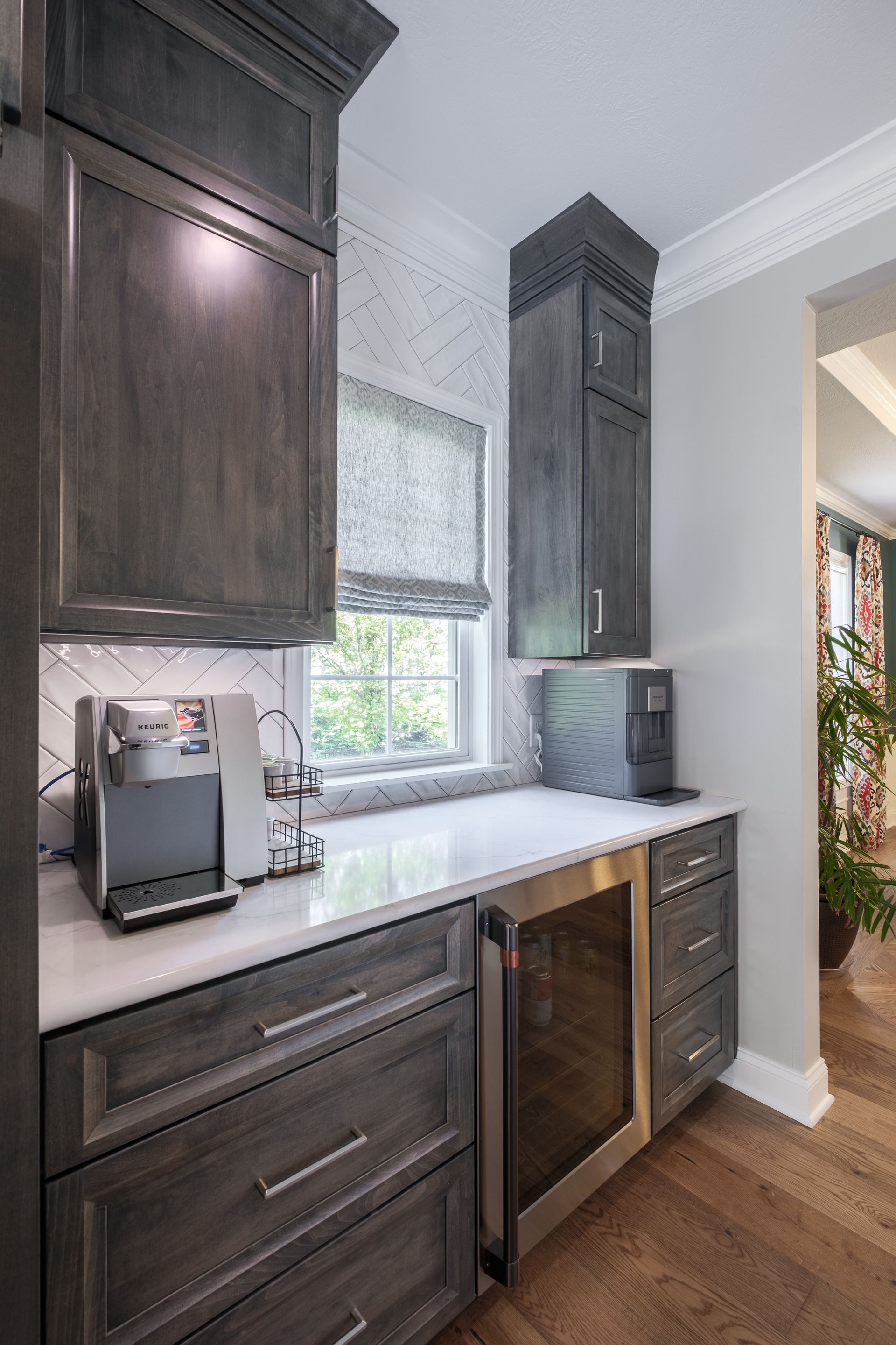Coffee station with dark gray cabinets, marble counter, window, and wine cooler.