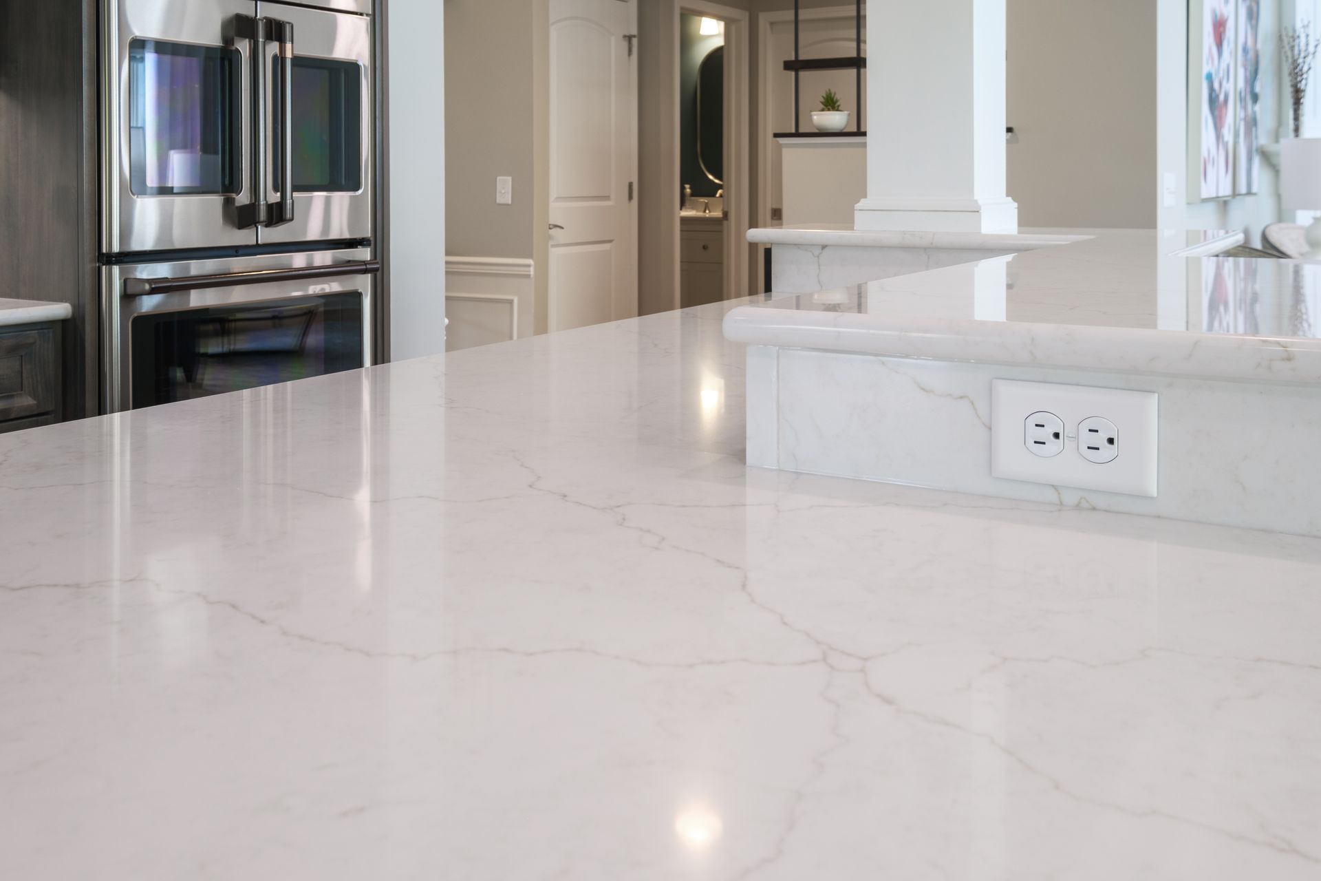 White quartz countertop with electrical outlet; stainless steel oven in background.