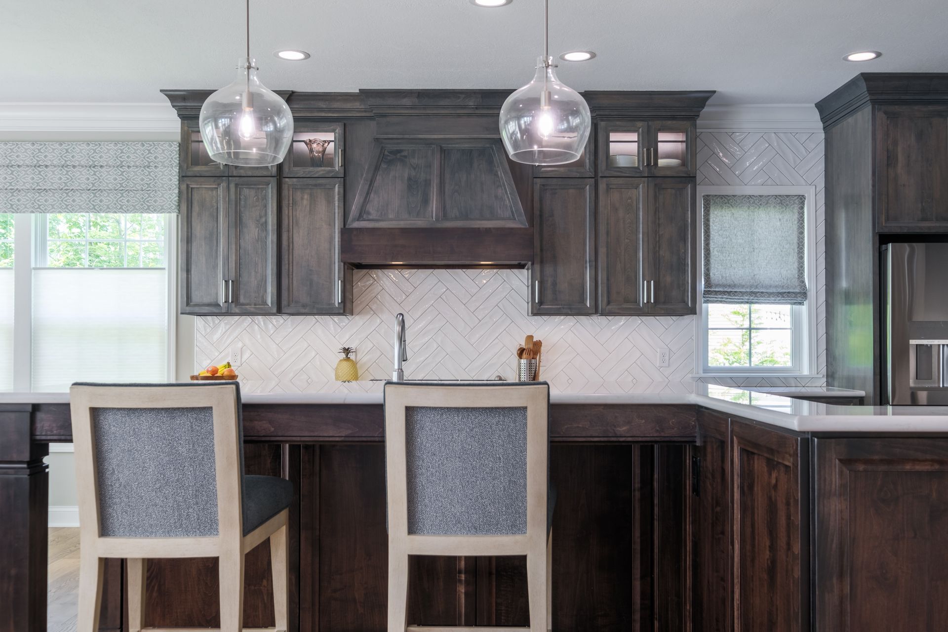 Modern kitchen with gray cabinets, marble backsplash, and two pendant lights. Two bar stools.