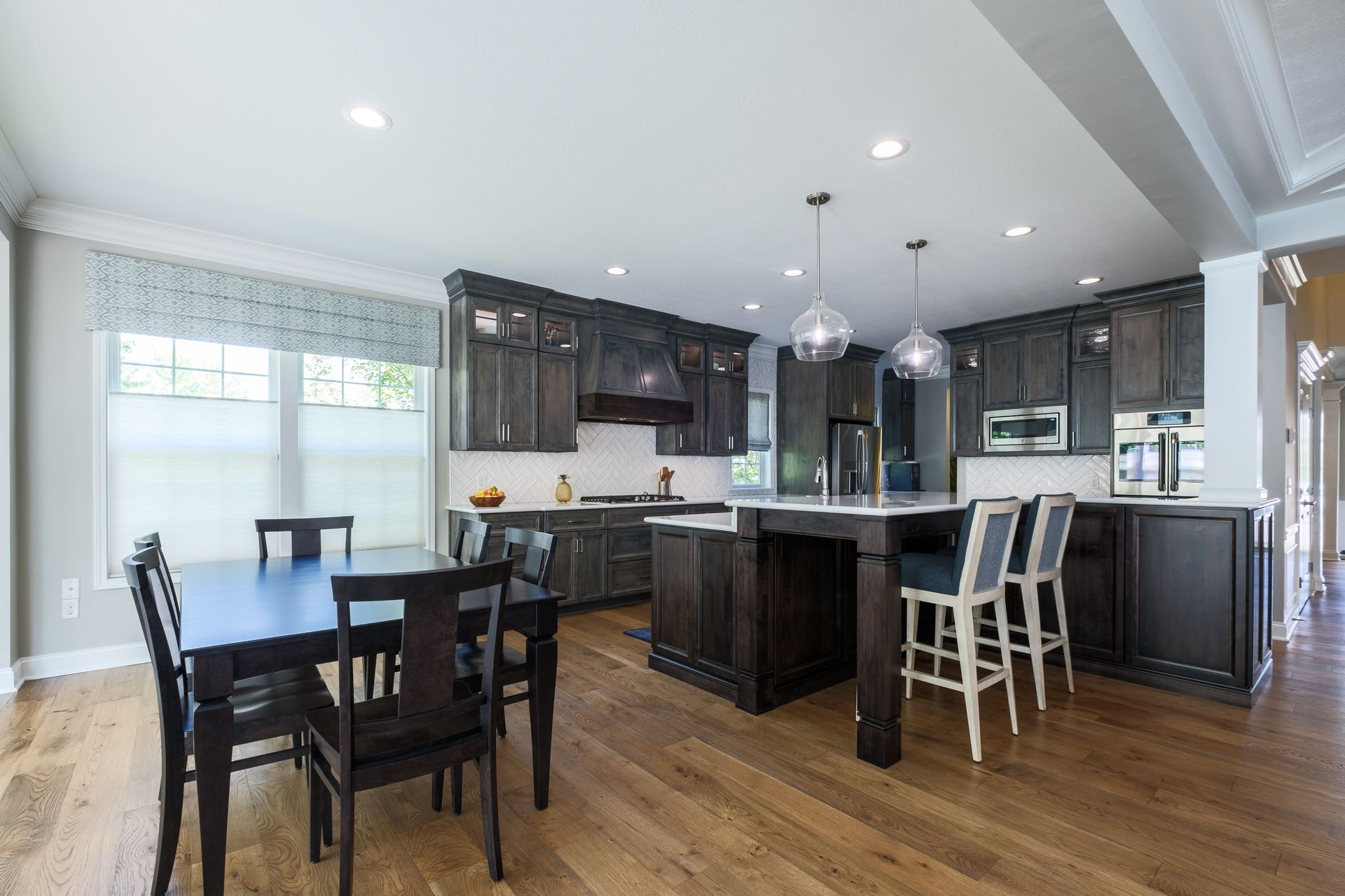 Dark wood kitchen with island, table, and chairs. Overhead lights and windows.