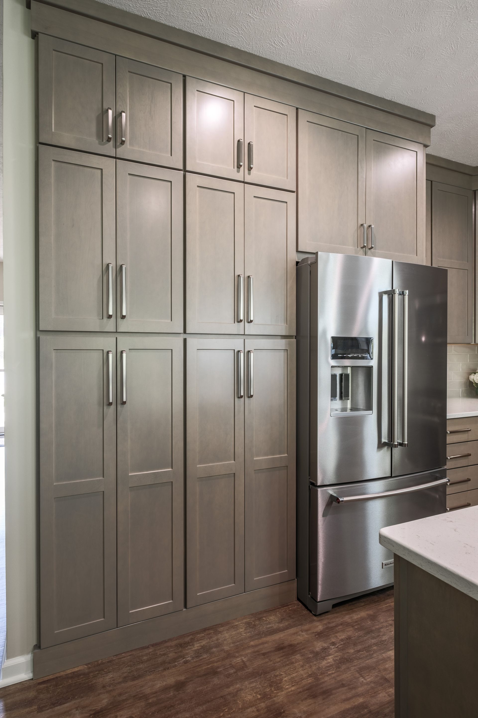 Tall, gray kitchen cabinets and stainless steel refrigerator on brown flooring.