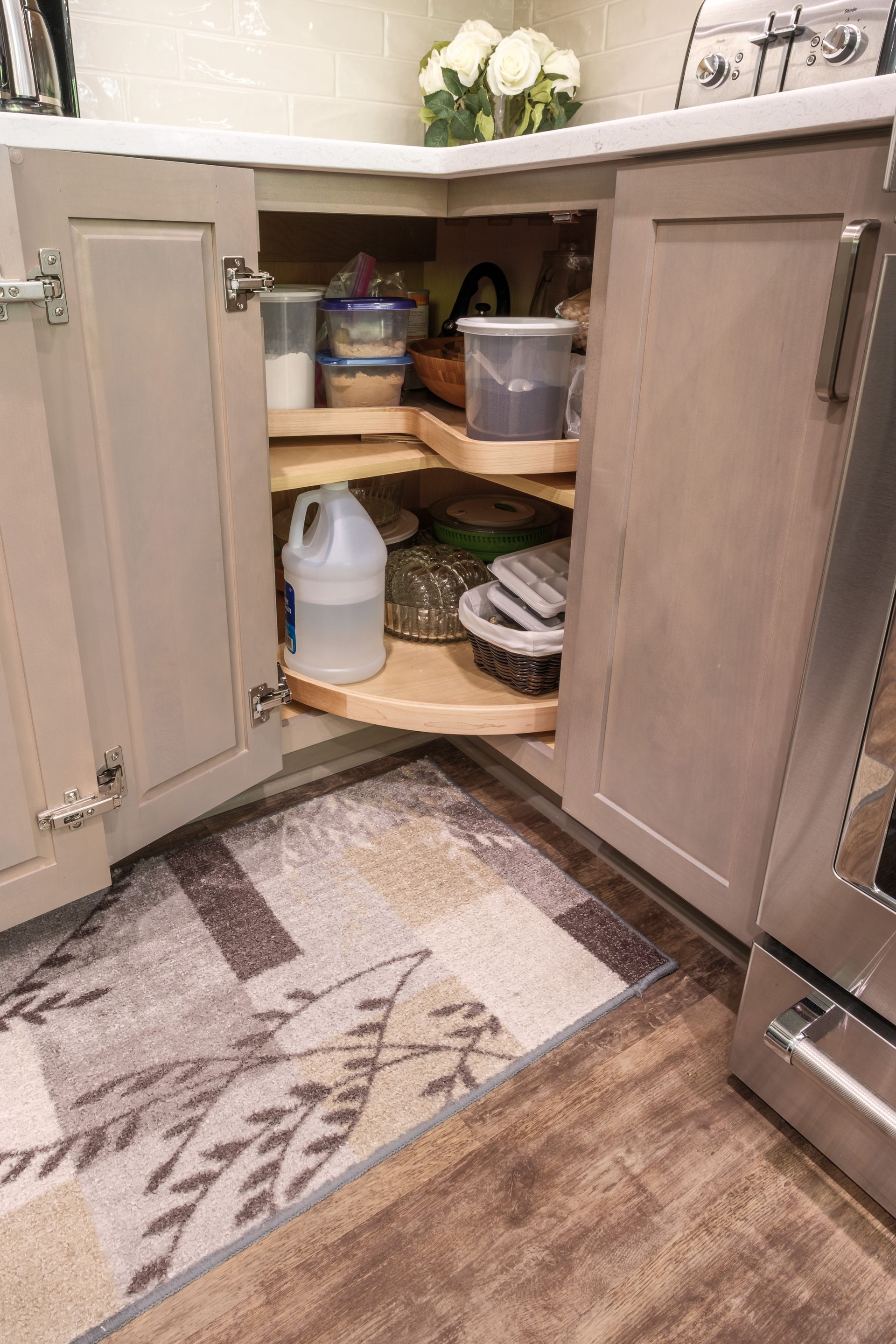 Corner kitchen cabinet with pull-out shelving, containing food and cleaning supplies. Includes a beige rug.