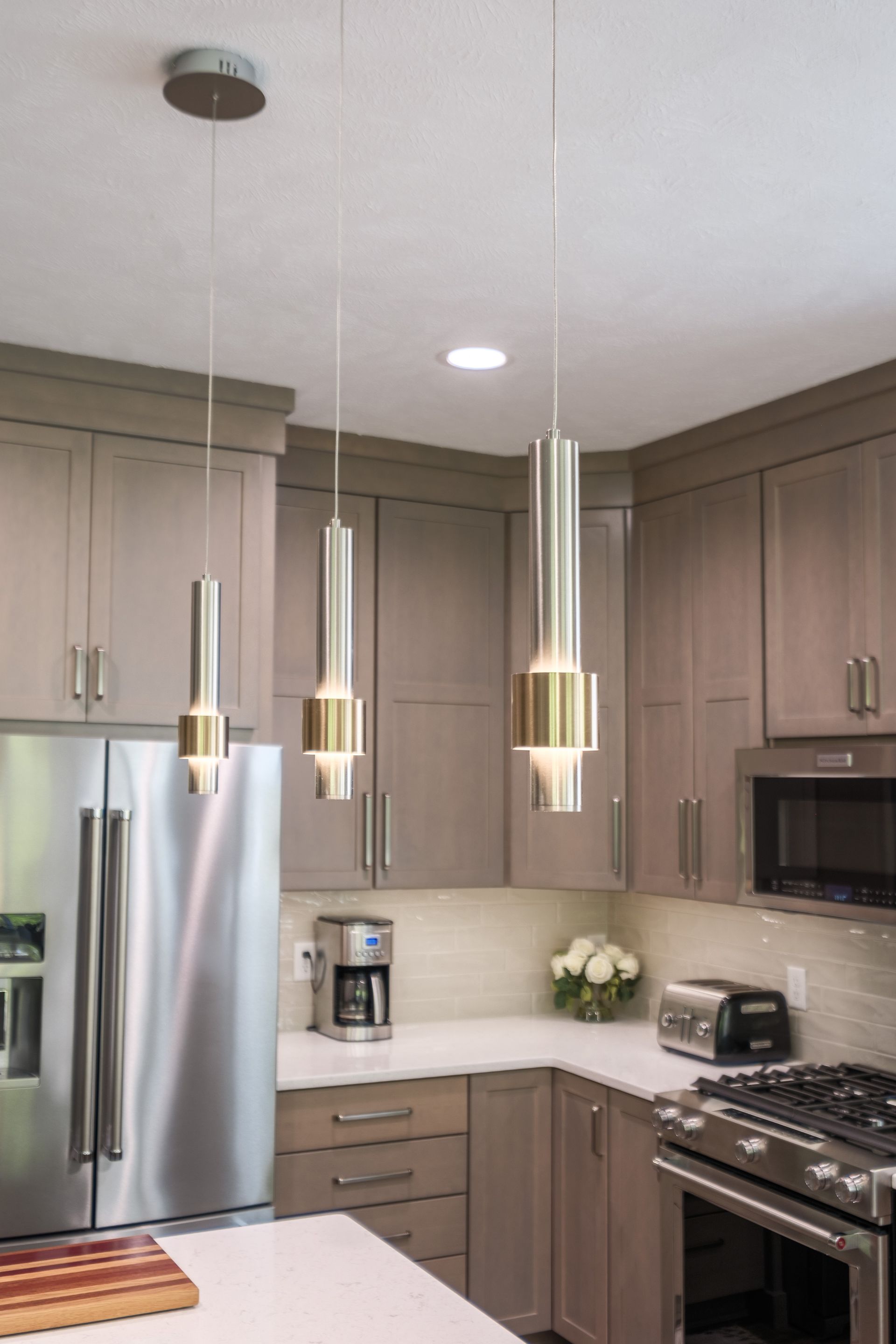 Kitchen with gray cabinets, stainless steel appliances, and modern pendant lights over a white countertop.