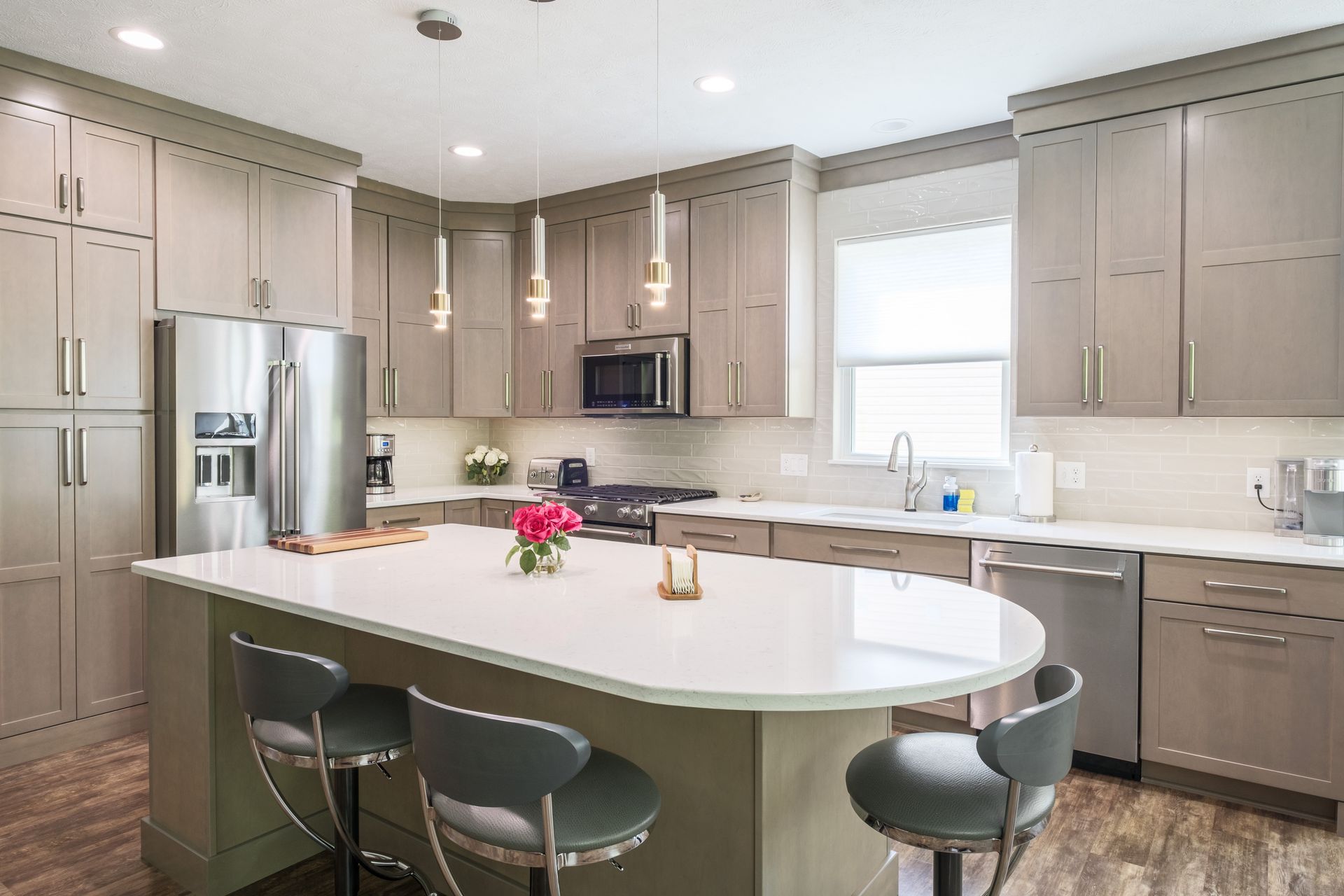 Modern kitchen with light gray cabinets, stainless steel appliances, and an island with bar stools.