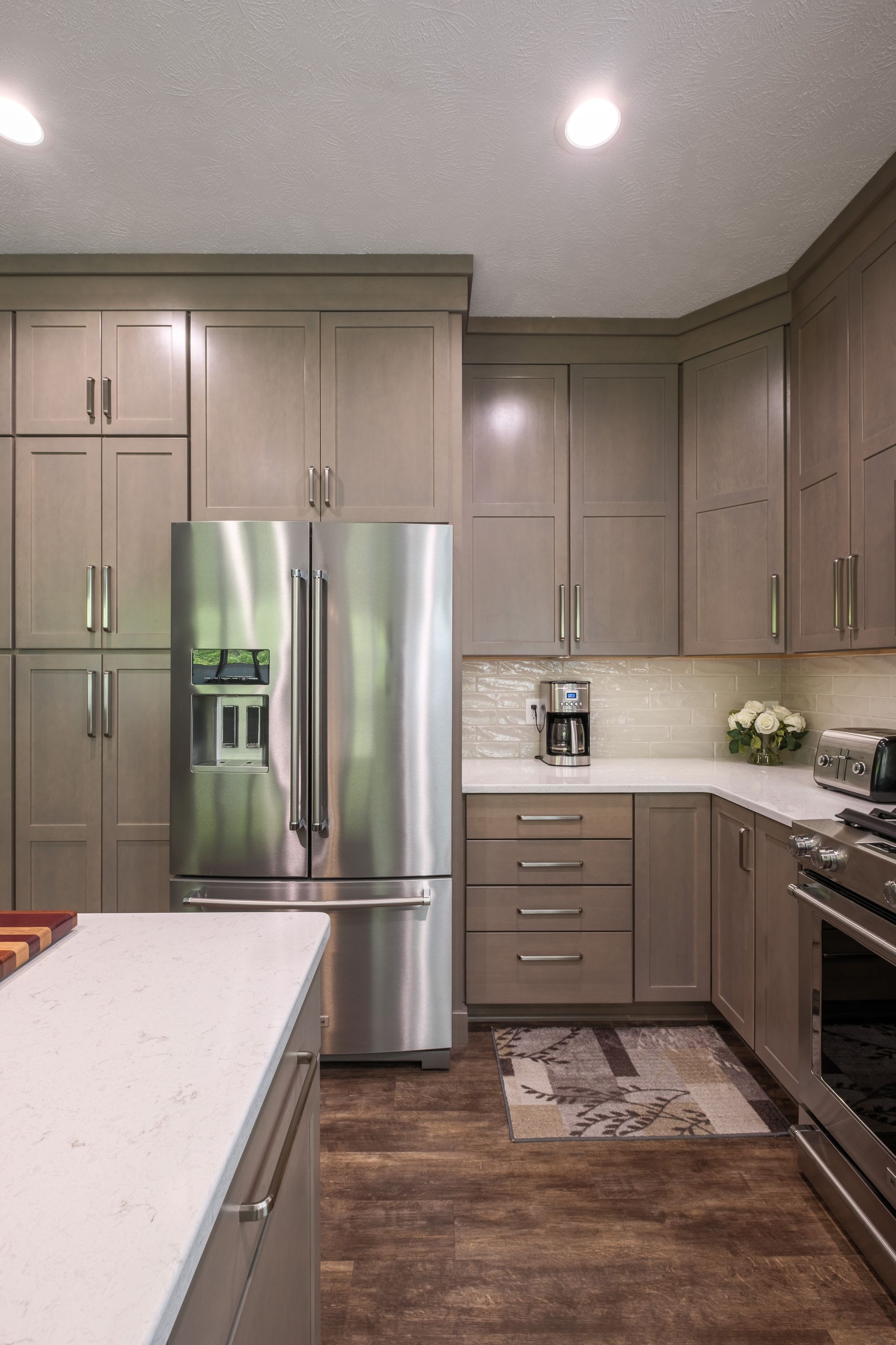Modern kitchen with gray cabinets, stainless steel fridge, white countertops, and wood floors.