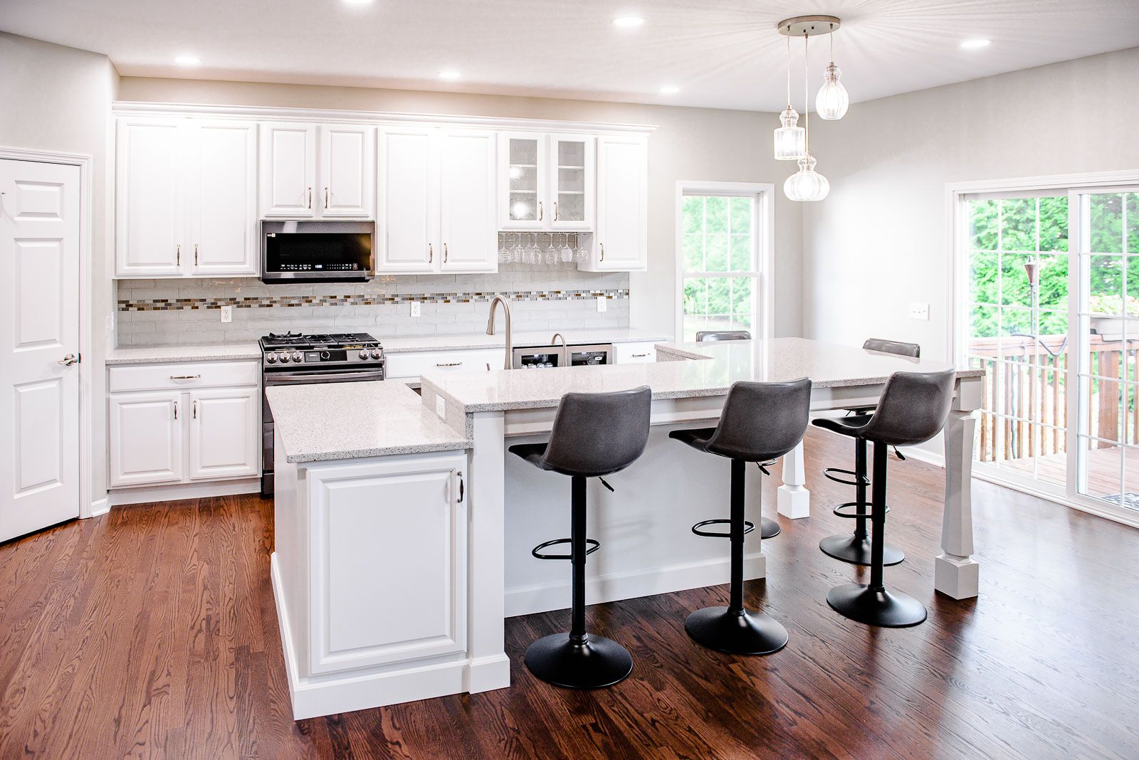 White kitchen with island, dark wood floor, and three gray bar stools.