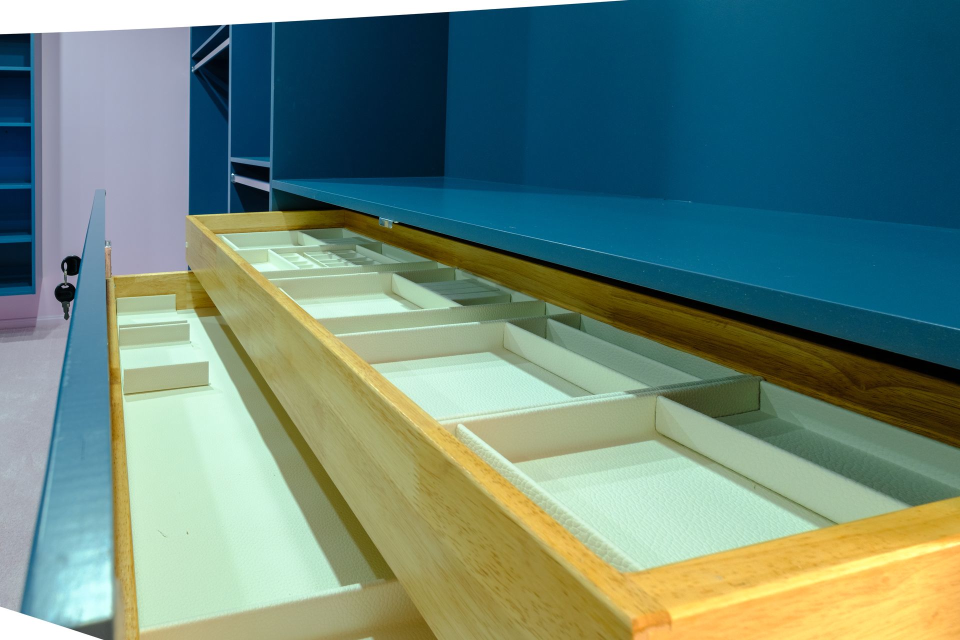 Open wooden drawer with beige dividers, set against blue cabinetry.