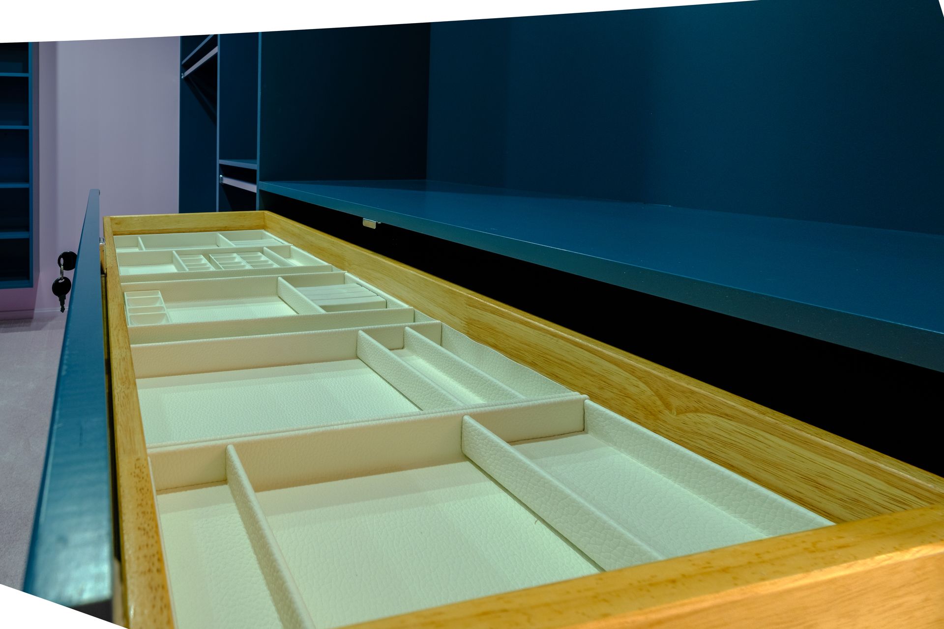 Open wooden drawer with beige compartments, set against a dark blue shelf and cabinets.
