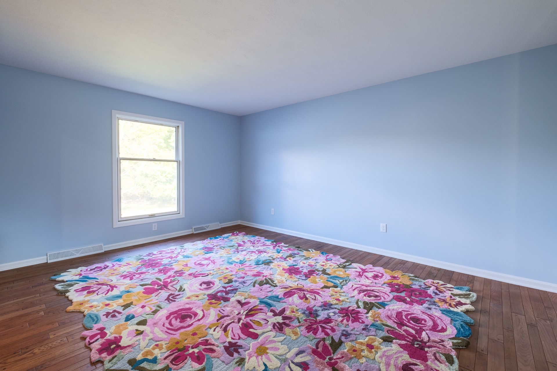 Room with hardwood floor, light blue walls, a window, and a large floral rug.