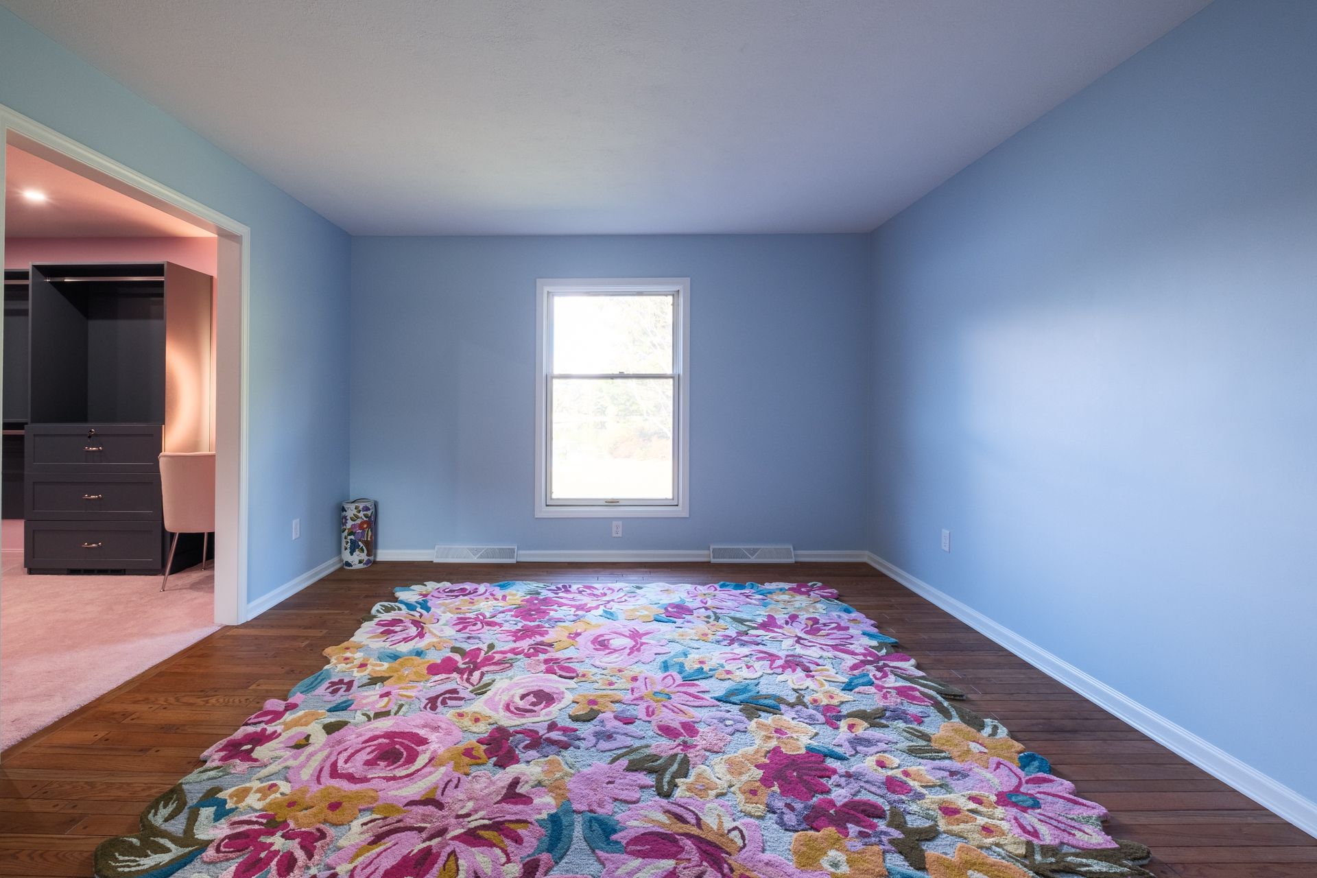 Empty room with blue walls, hardwood floor, floral rug, and a window. A closet is visible in the doorway.
