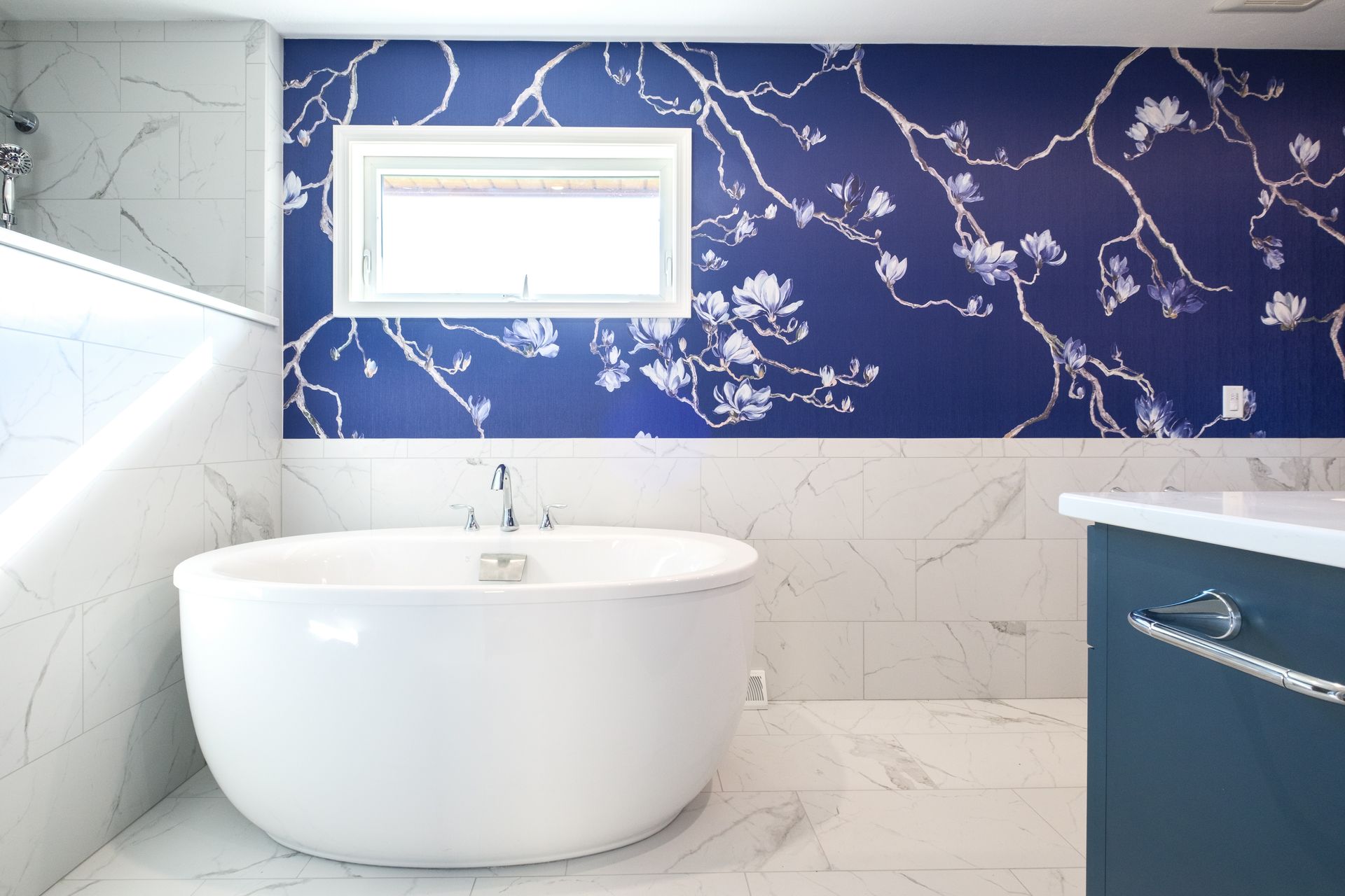 Bathroom with a white tub, blue floral wallpaper, white marble walls, and blue vanity.