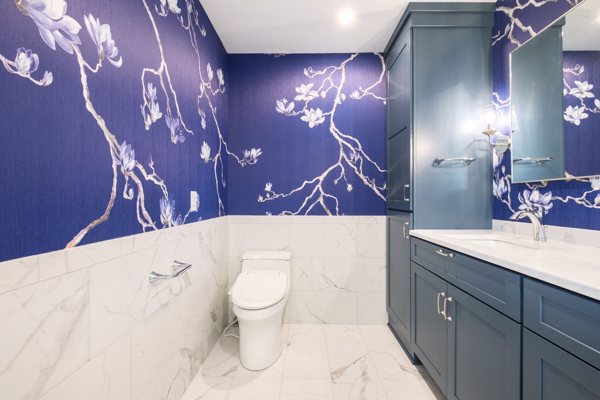 Bathroom with blue floral wallpaper, white marble tile, and blue vanity.