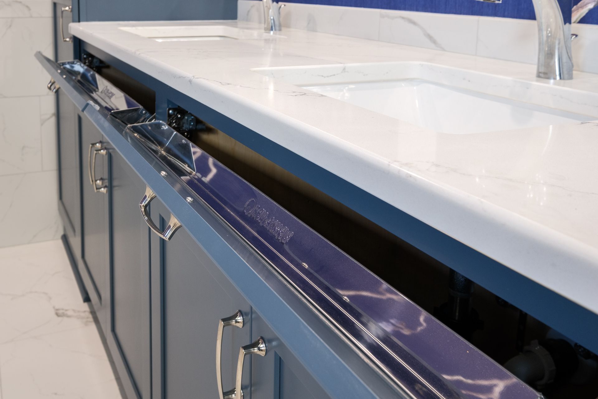 Blue bathroom vanity with open drawers, white countertop, two sinks, and chrome hardware.