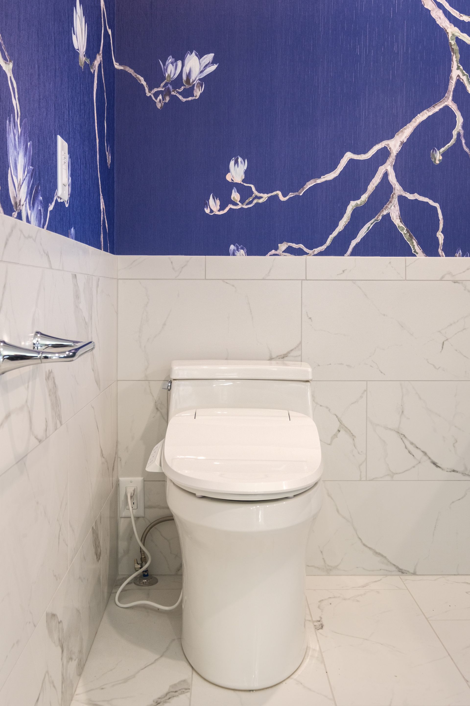 White toilet in a bathroom with white marble walls and blue floral wallpaper.