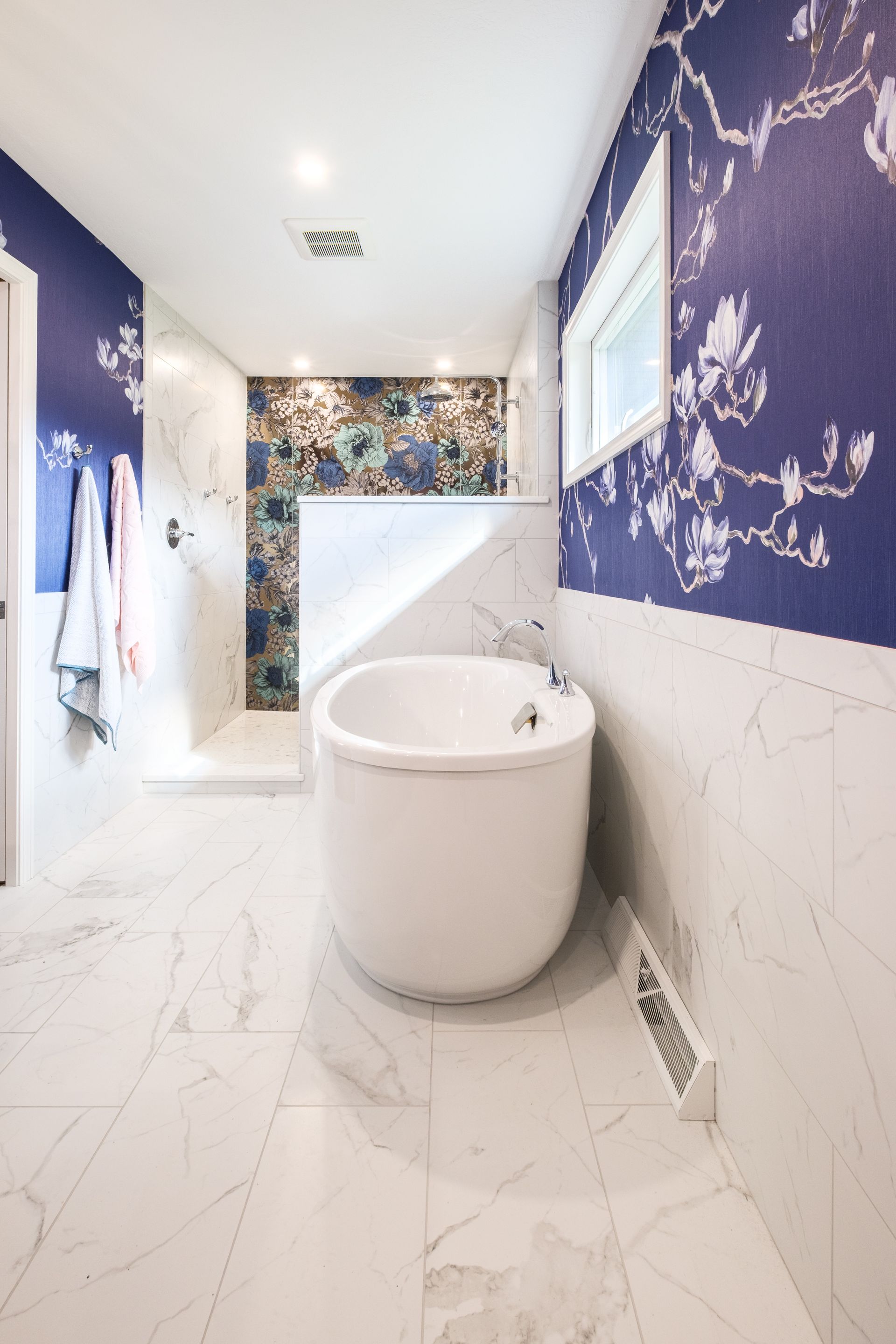 Modern bathroom with white tub, marble floors, blue floral wallpaper, and glass shower.