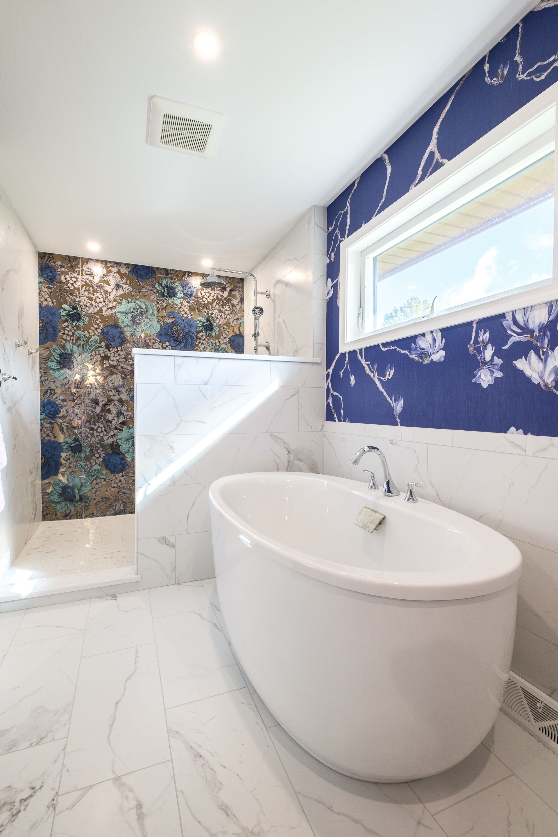 Modern bathroom with white marble, a blue floral accent wall, and a freestanding tub.