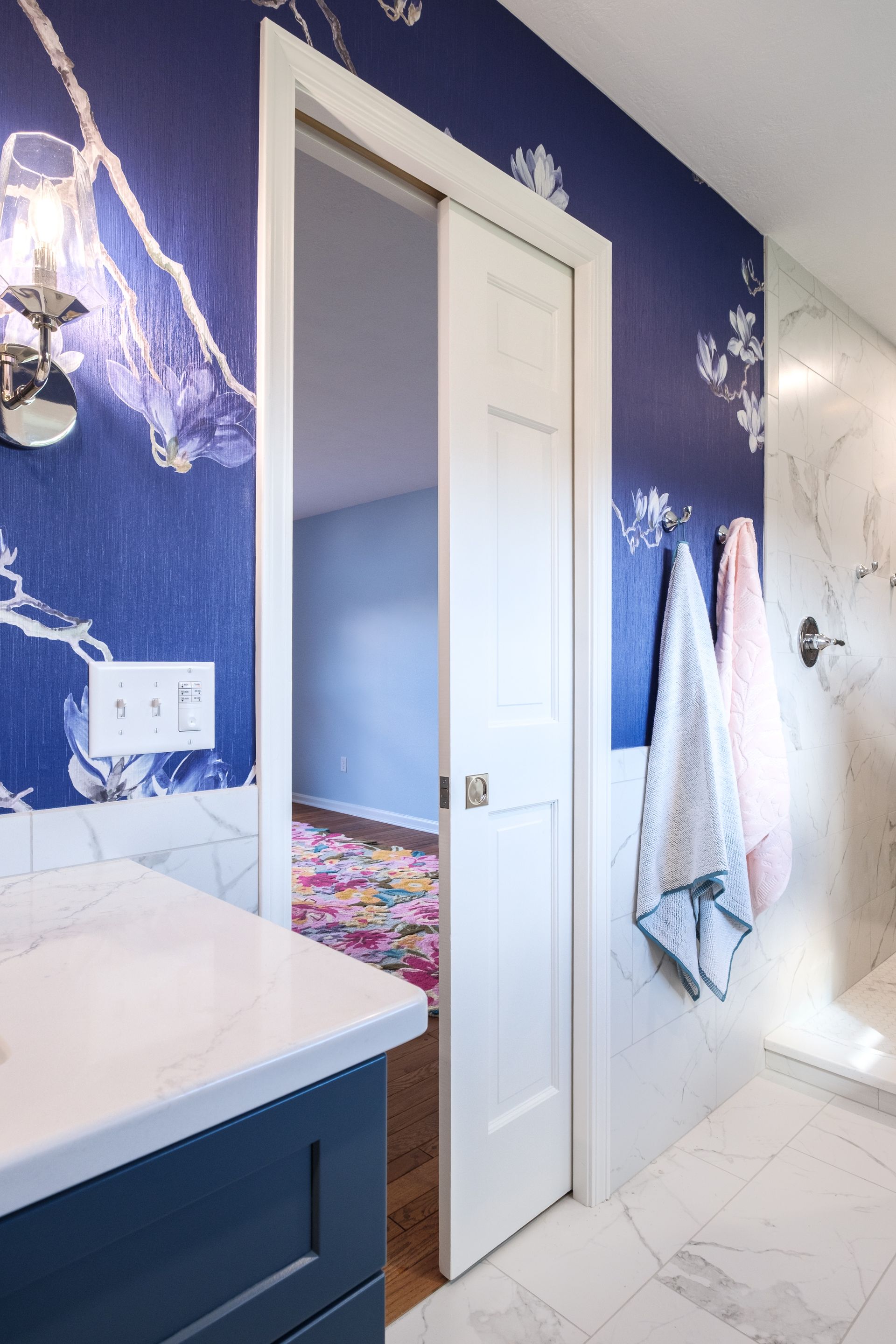 Bathroom with blue floral wallpaper, white door, marble shower, and vanity.
